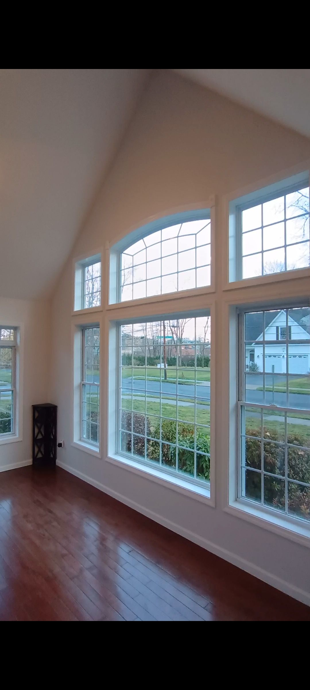 Living room with hardwood floors, large windows with a view of green grass and trees.