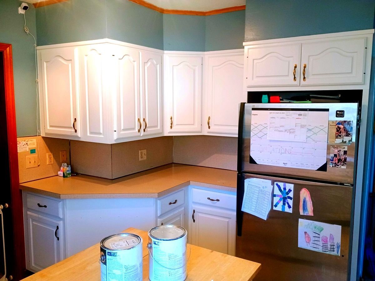 Kitchen with white cabinets, light countertops, stainless steel fridge, and paint cans on island.
