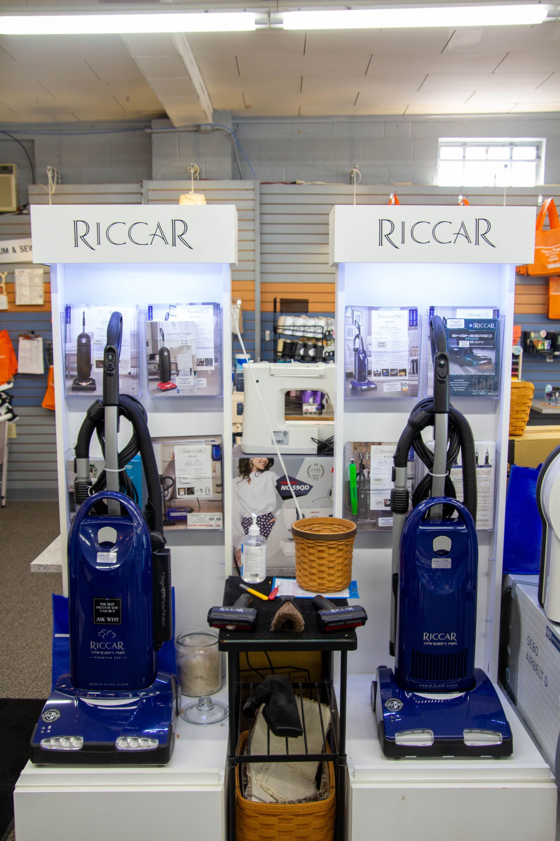 Two blue Riccar vacuum cleaners displayed on a store shelf, with informational signs.