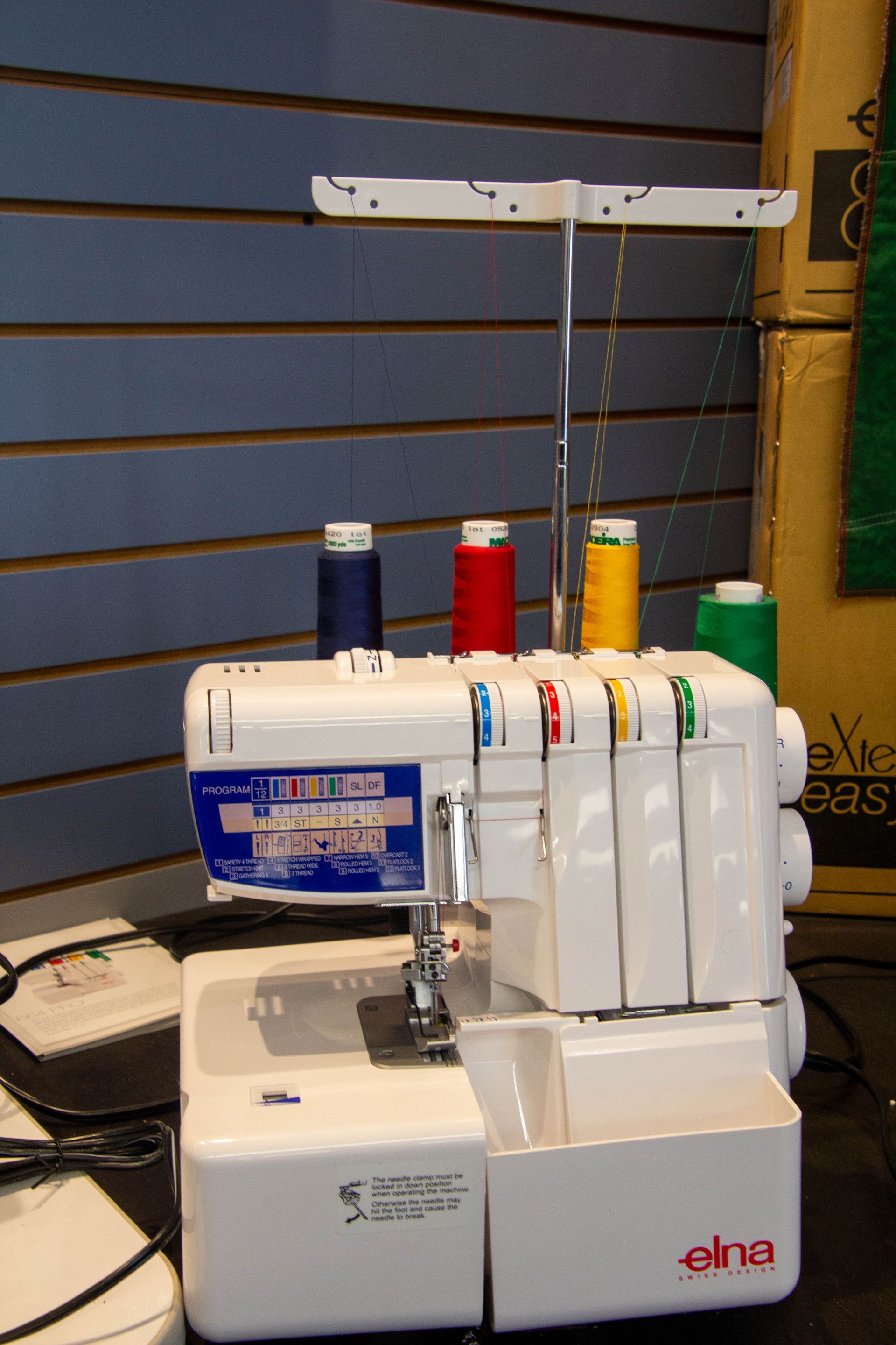 White Elna serger with spools of blue, red, yellow, and green thread.
