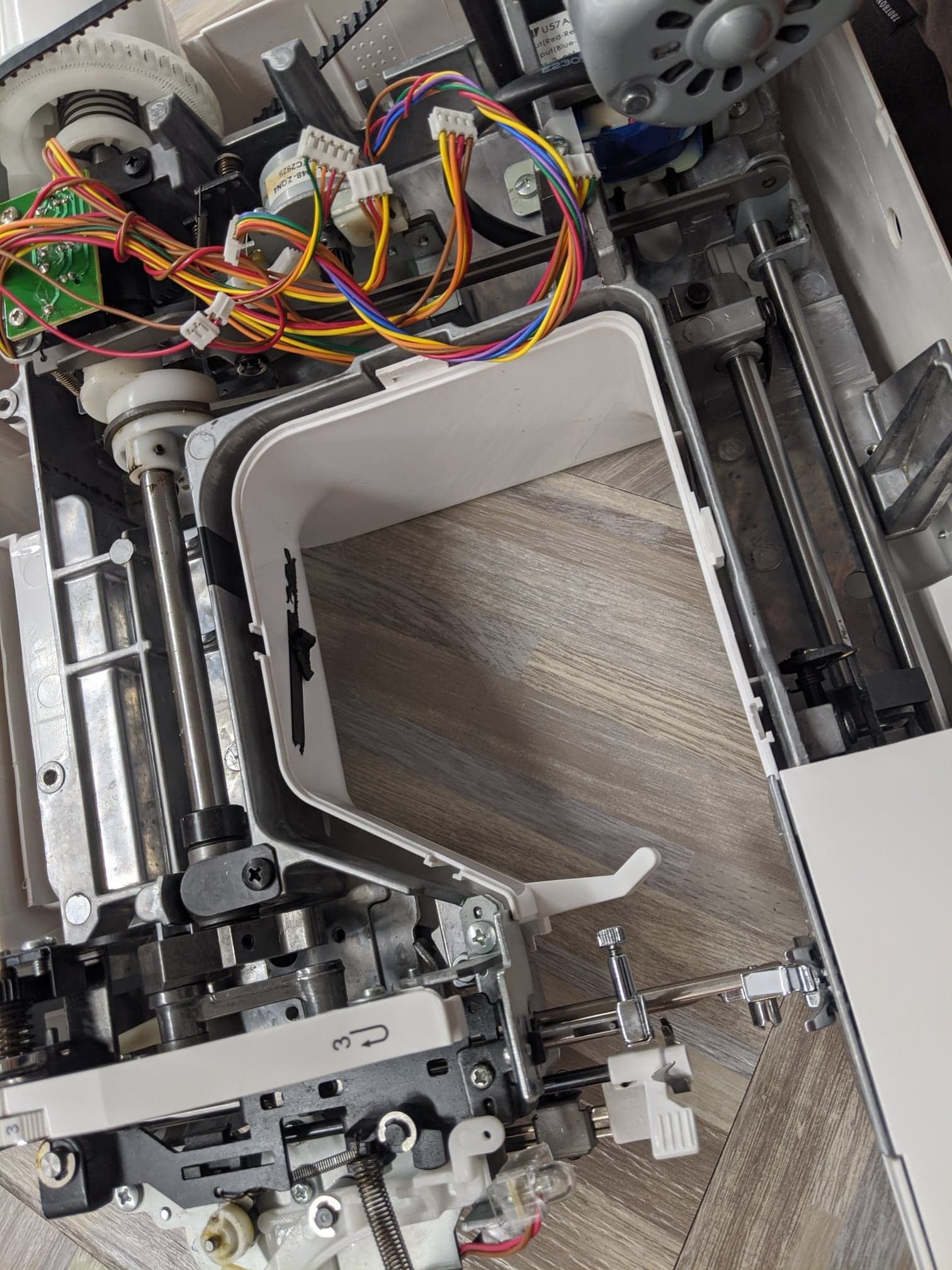 Open sewing machine, showing internal mechanisms including wires, motors, and metal parts.