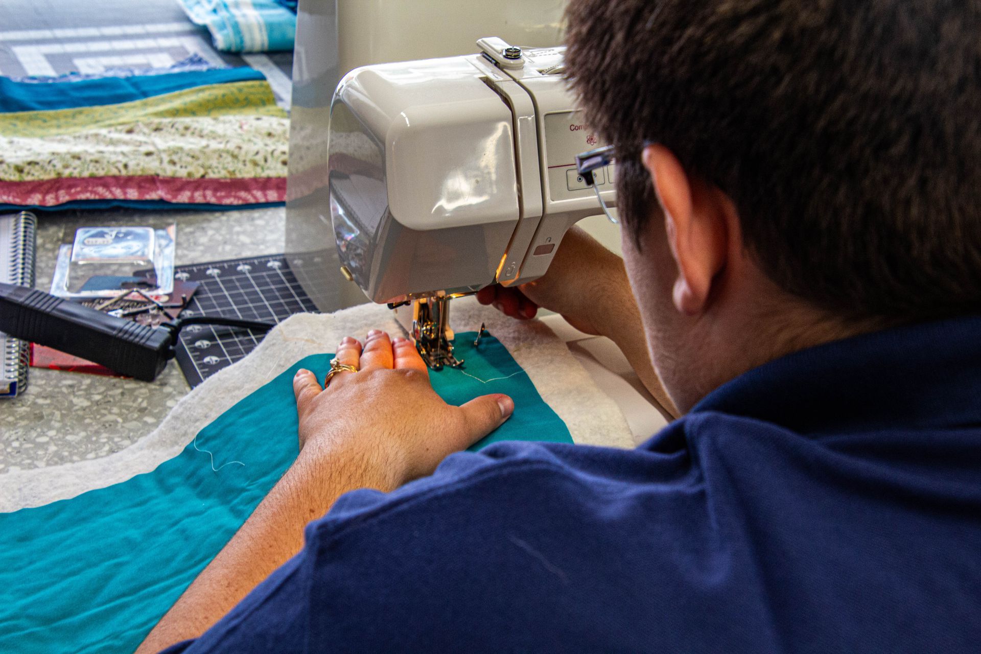 Person sewing on a white machine; blue fabric being stitched, close up of hands and sewing area.