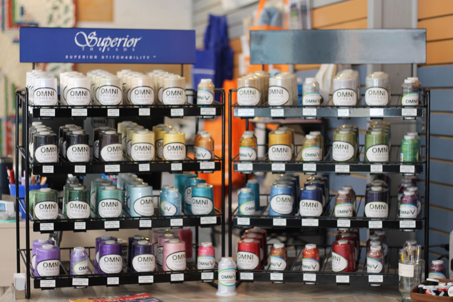 Display of embroidery thread spools in a store, arranged by color on a black metal shelf.