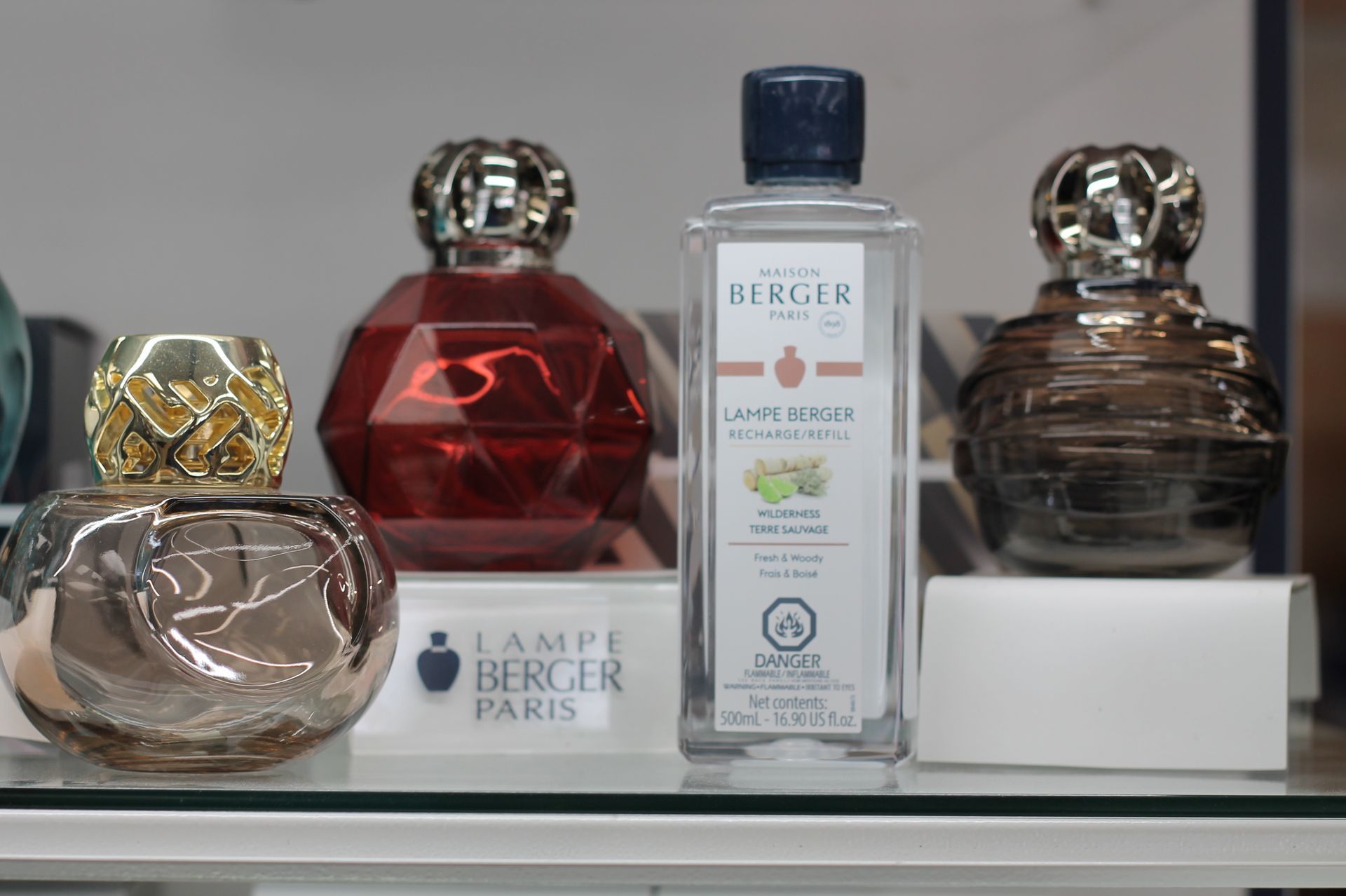 Lampe Berger products on a shelf. Three glass lamps, one bottle of fragrance.