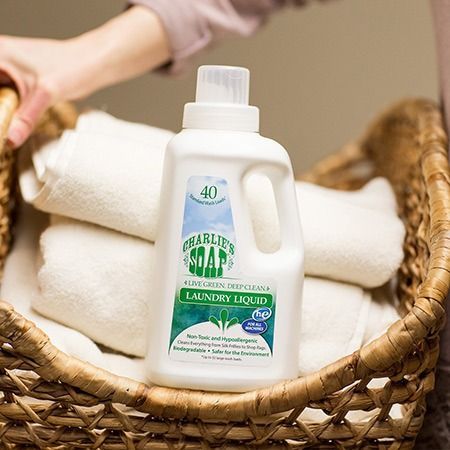 Laundry detergent bottle in a basket of folded white towels. Hand reaching in.