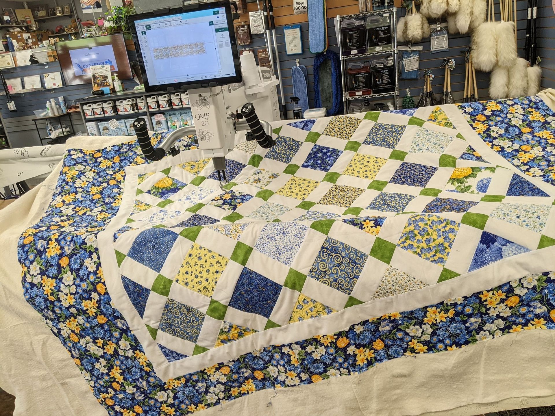 Quilting machine in a shop with a colorful diamond-patterned quilt and floral border.