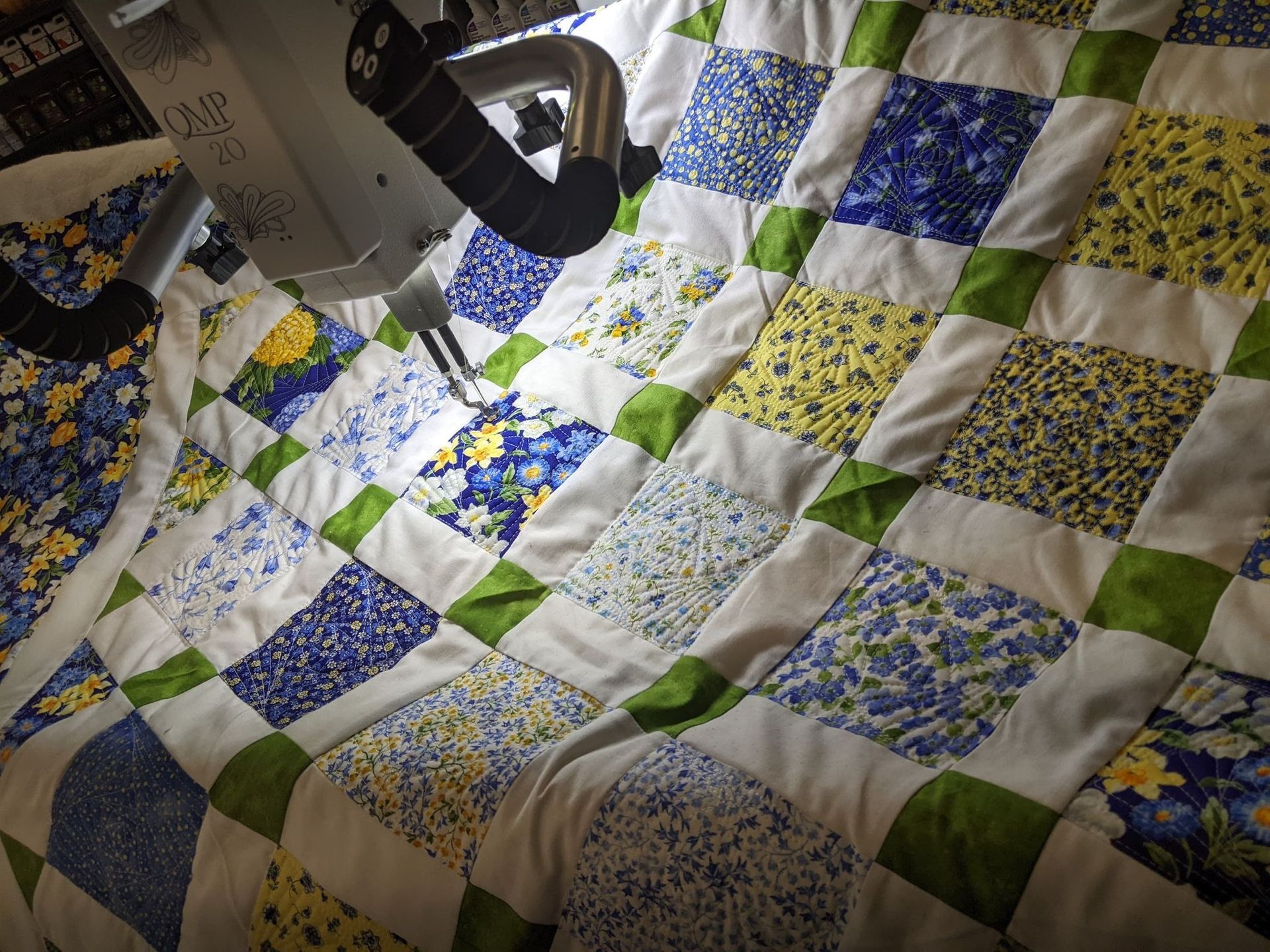 Machine quilting a patchwork quilt with blue, yellow, and green squares.