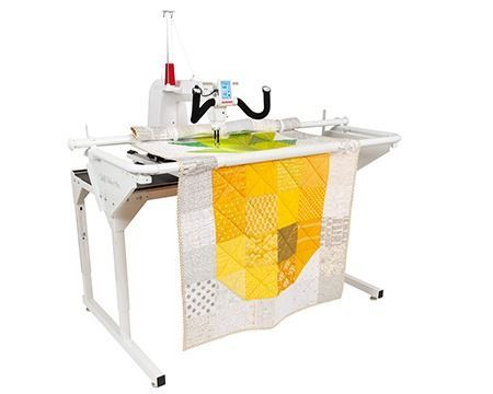 White quilting machine with a yellow and gray quilt in progress on a table.