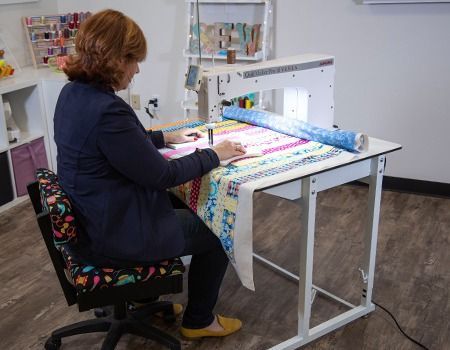 Woman sewing quilt on a long arm machine in a bright craft room.