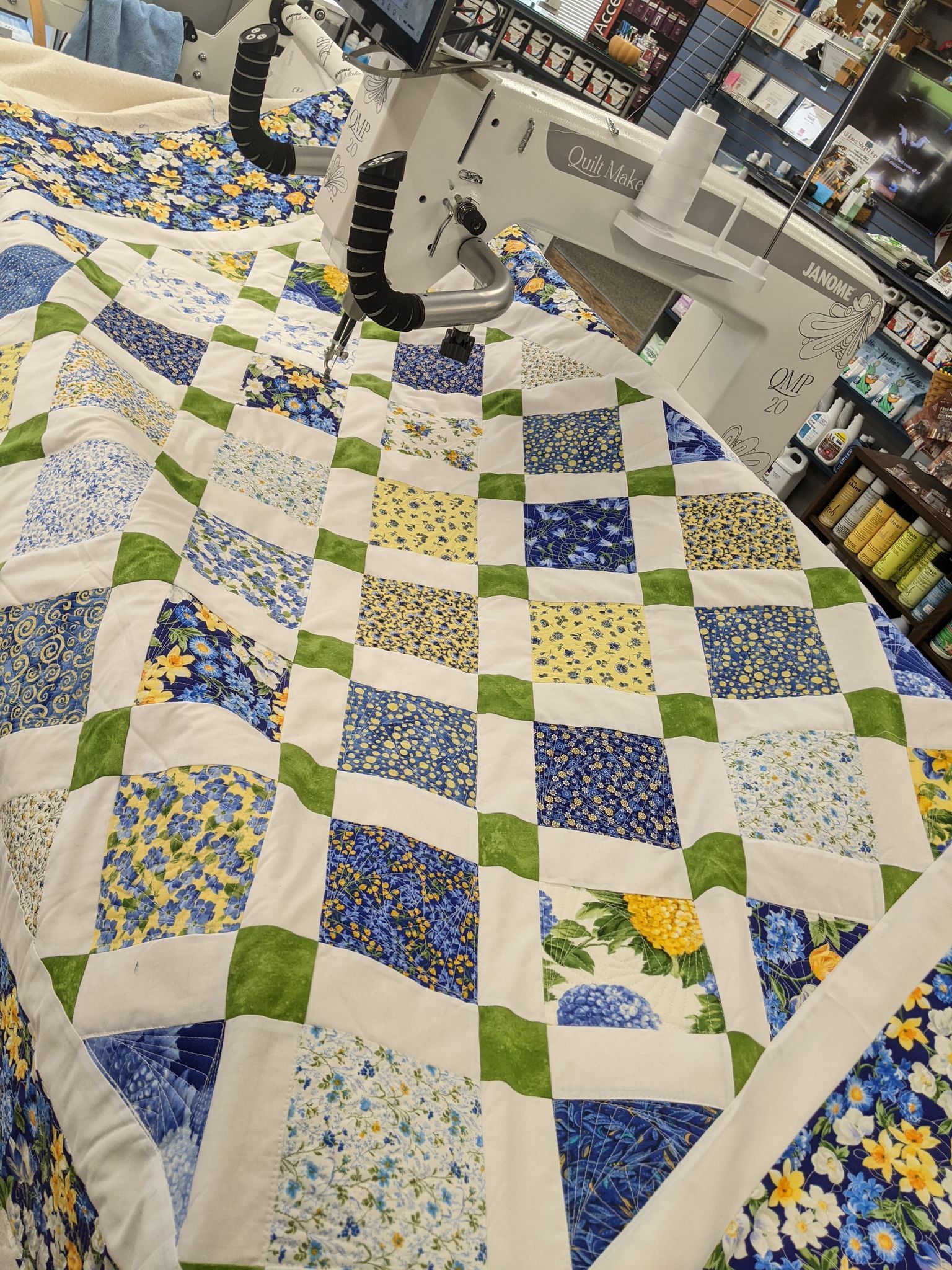 Quilt being stitched by a machine. Blue, green, and yellow floral fabric with white borders.
