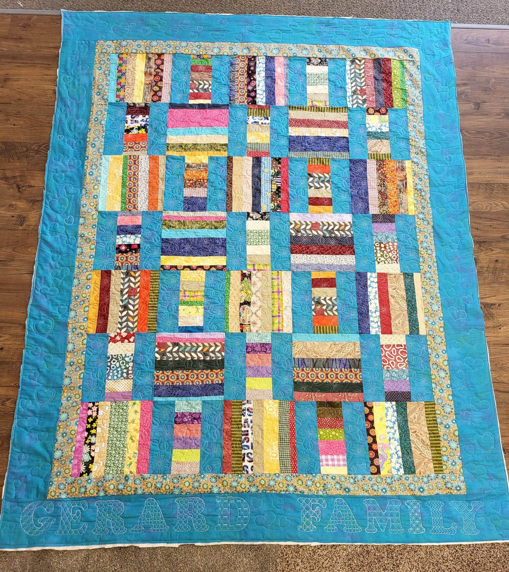 Colorful patchwork quilt with turquoise border on wood floor.