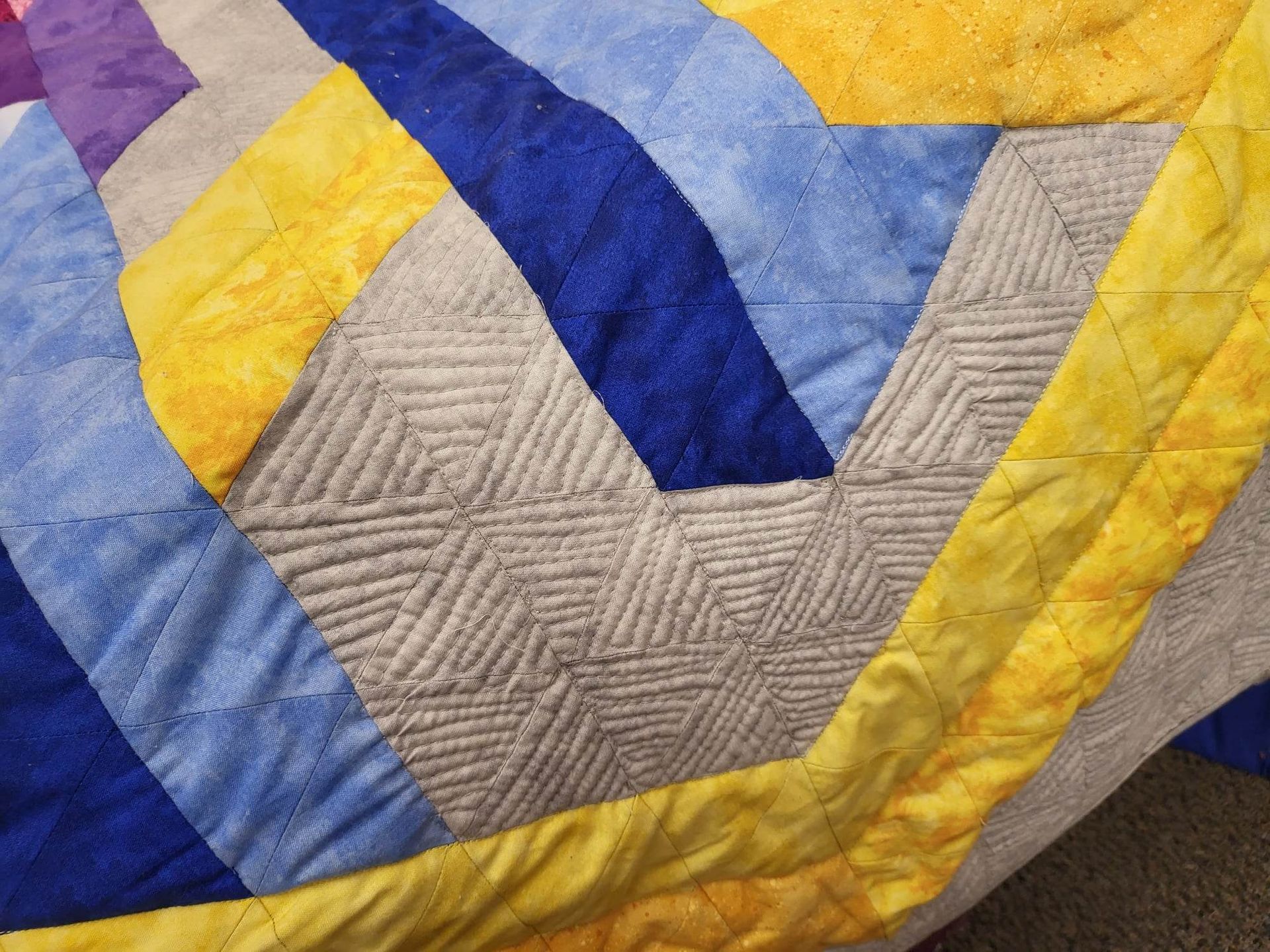 Close-up of a colorful quilt with geometric patterns in yellow, blue, and gray, with textured stitching.