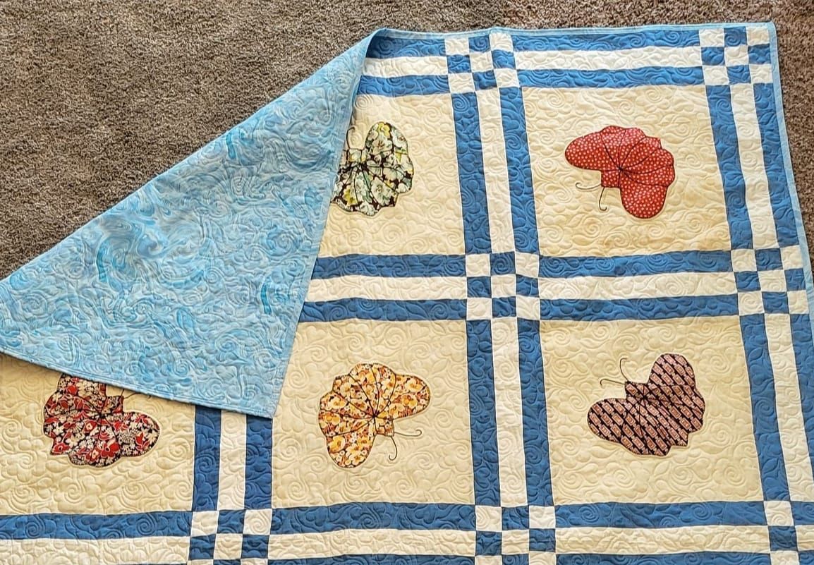 Quilt with blue and tan squares, four colorful appliquéd shapes, and a blue patterned backing.