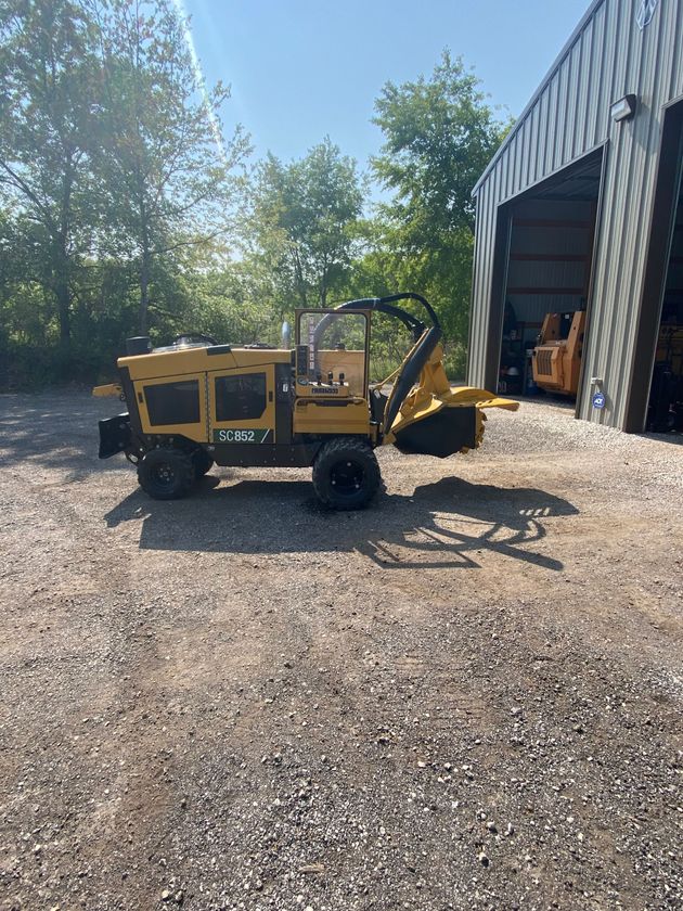 Yellow utility cart on gravel beside a metal building, with trees and a bright blue sky in the background.