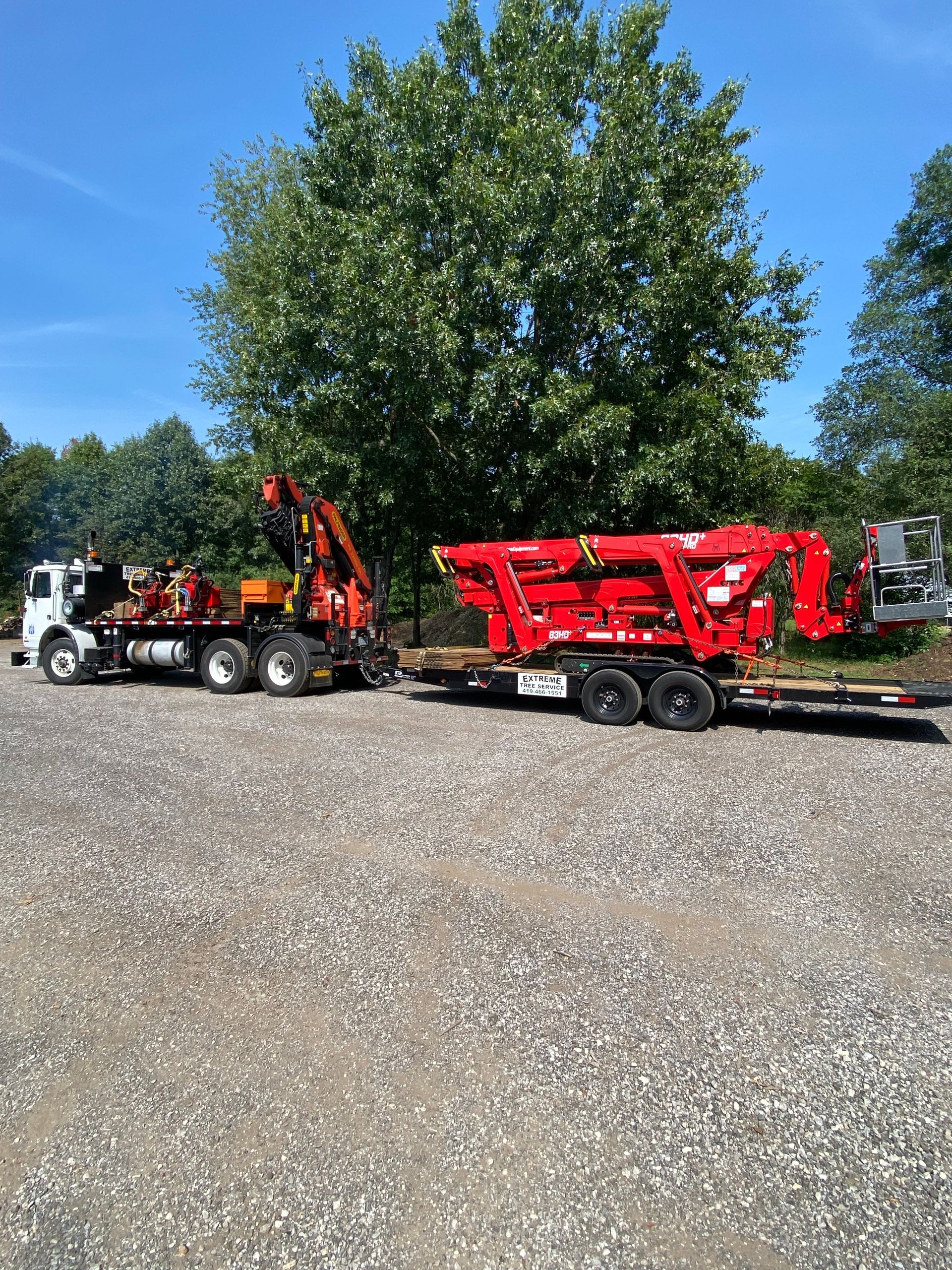 Black truck towing a red trailer in a gravel lot under a clear blue sky.