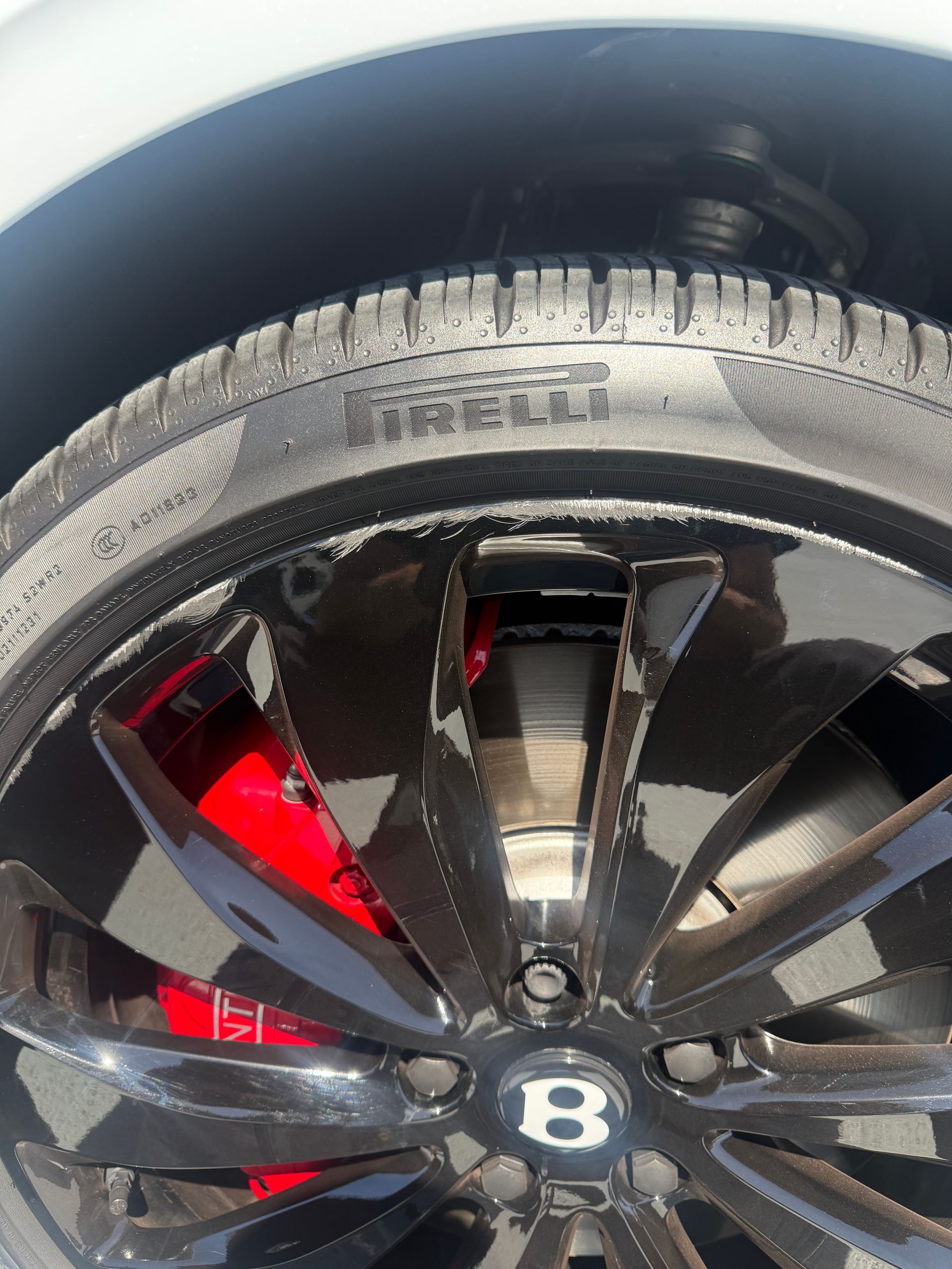 Close-up of a black Bentley wheel rim with red brake caliper and tire tread details.