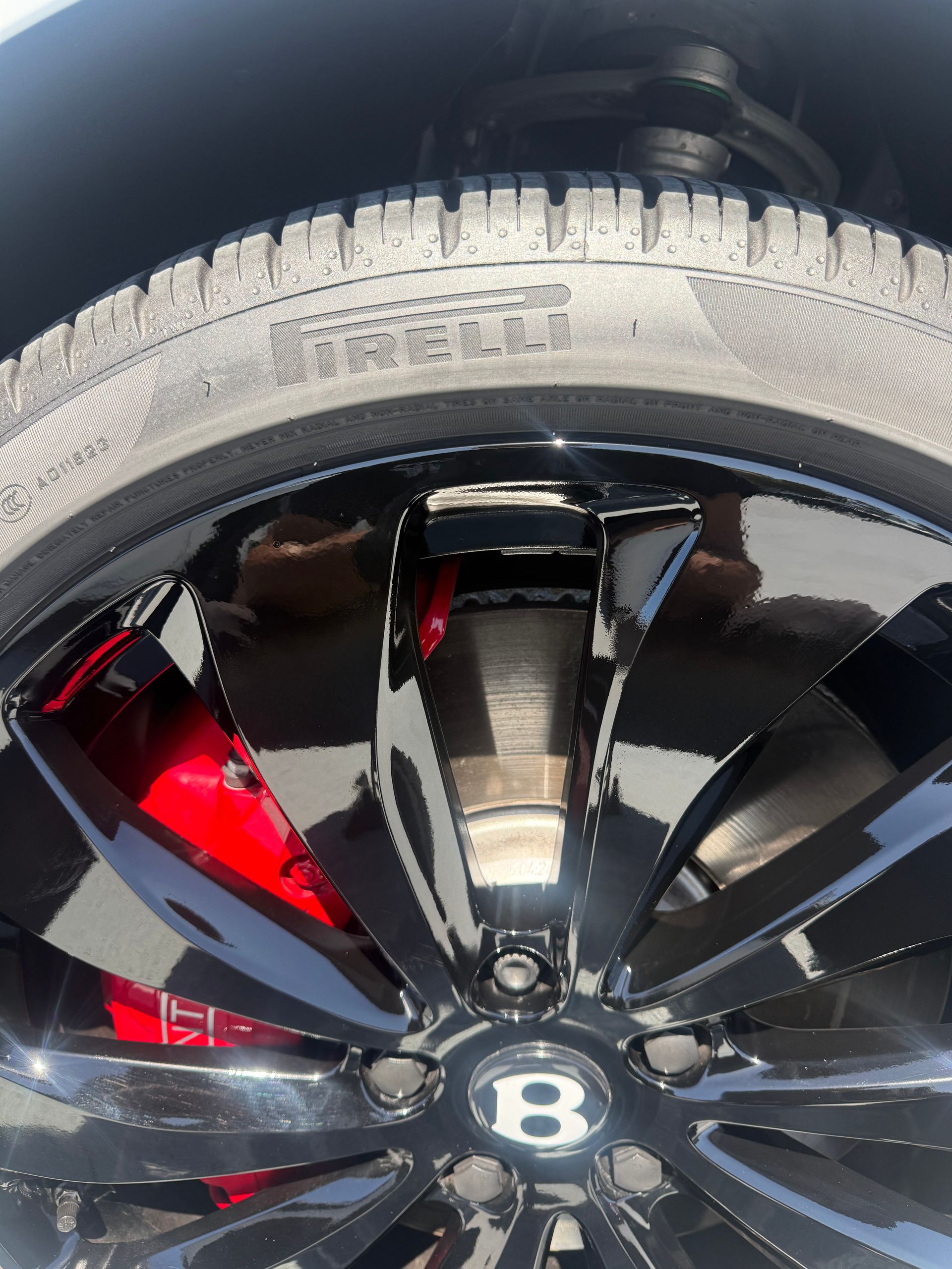 Close-up of a black Bentley wheel with a red brake caliper and tire tread visible.