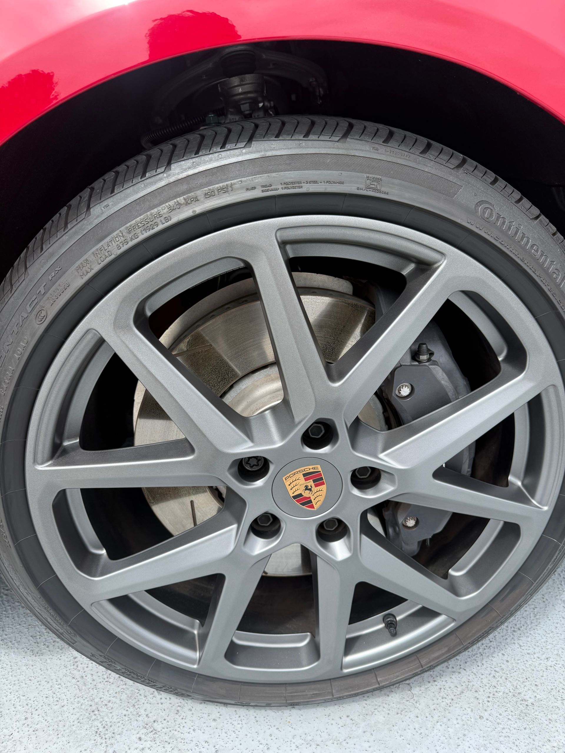 Close-up of a silver Porsche wheel and tire on a red car body.