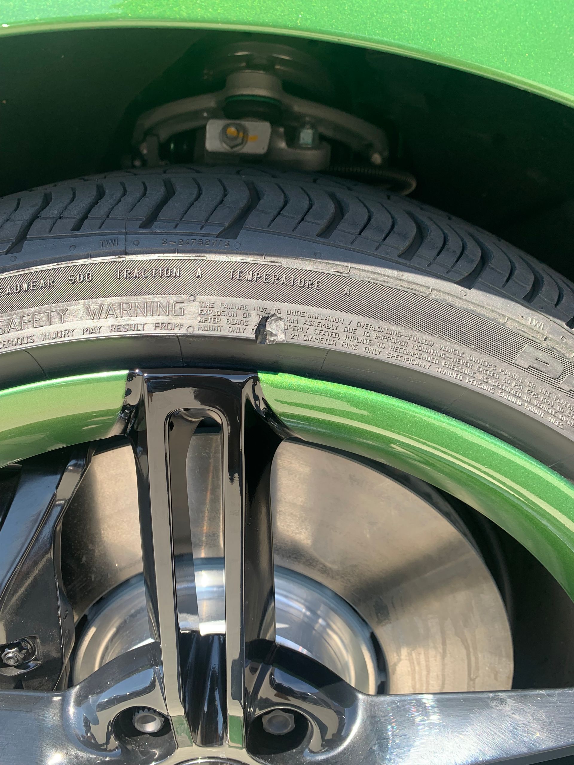Close-up of a car wheel, tire, and green rim inside the wheel well.