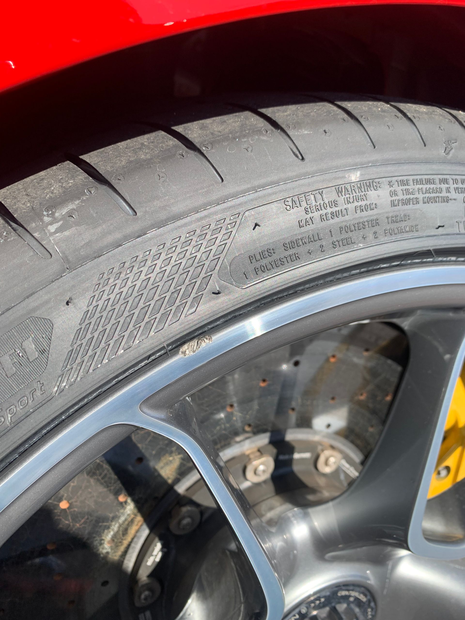 Close-up of a car wheel and tire on a red vehicle, showing tread and alloy rim details.