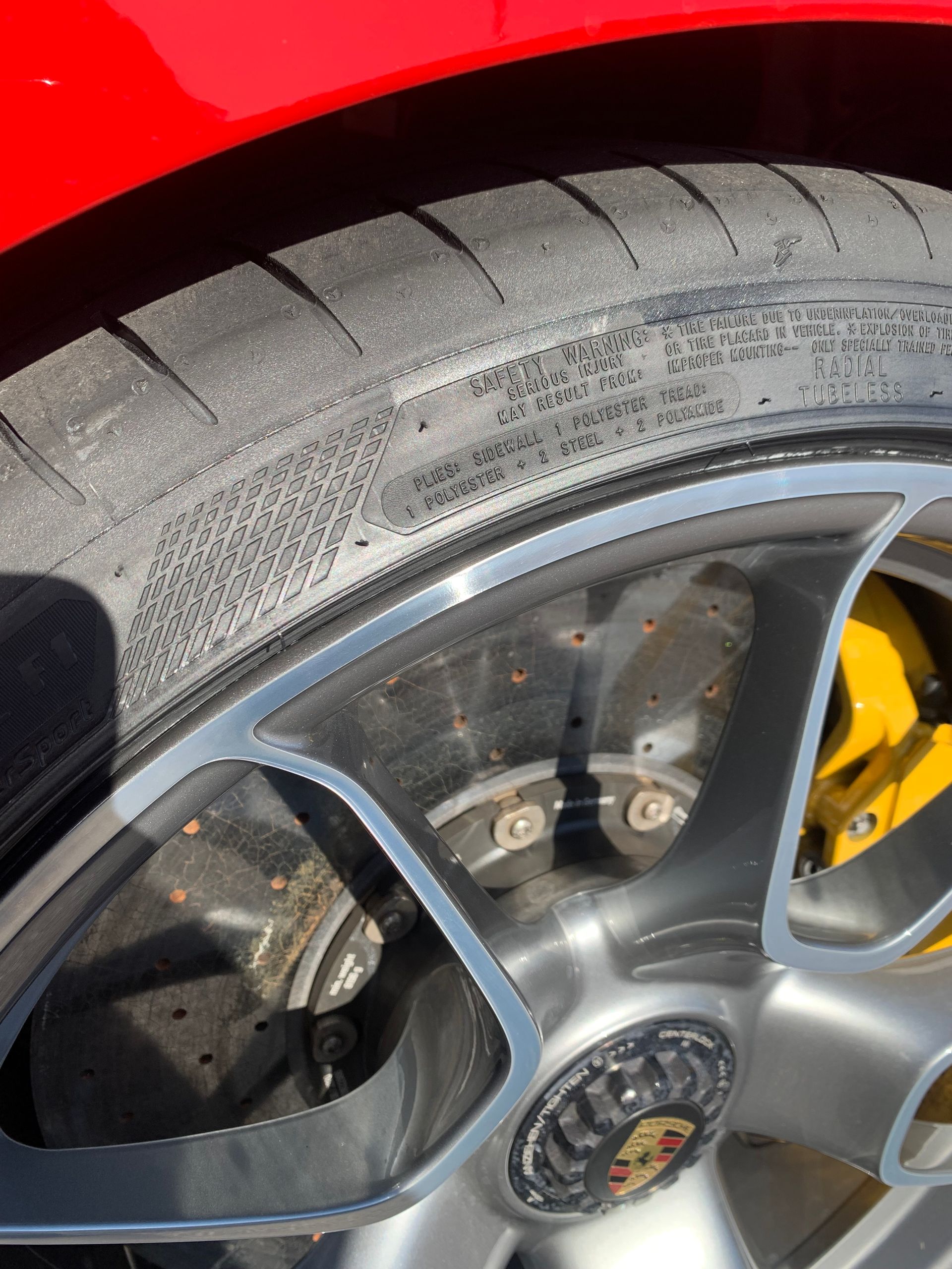 Close-up of a red sports car wheel with gray rim, yellow brake caliper, and worn tire.