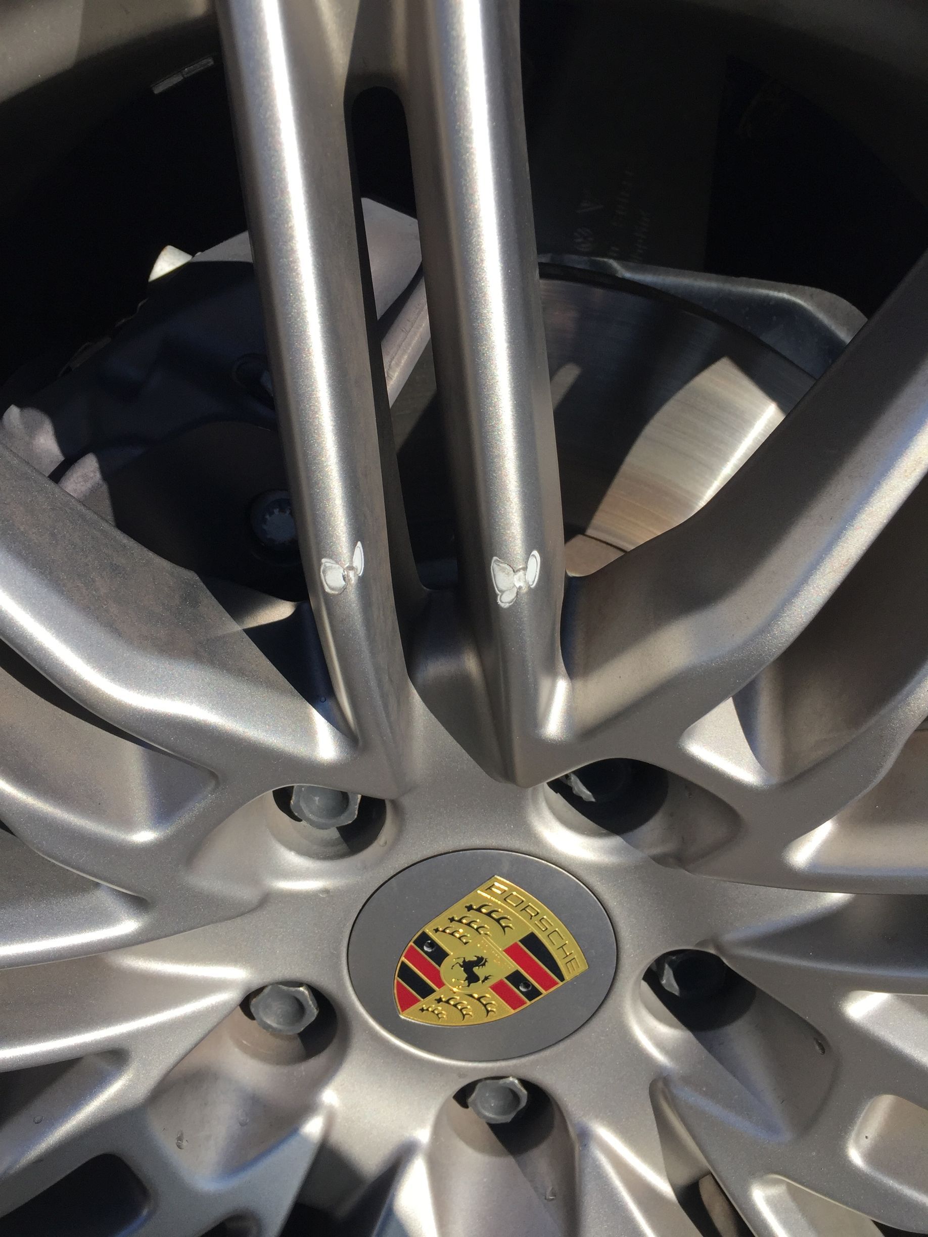 Close-up of a silver Porsche wheel rim with center crest and visible lug nuts.