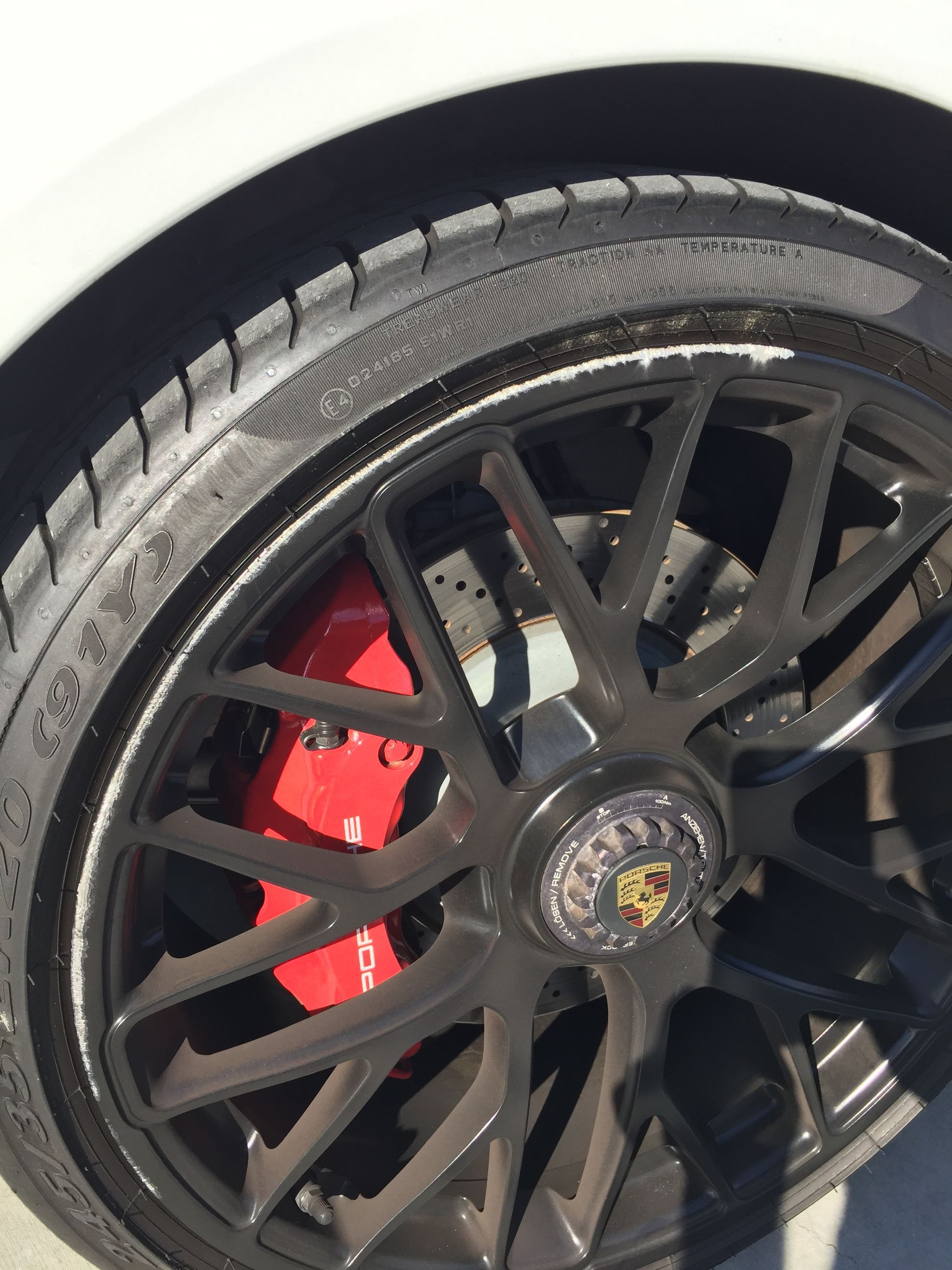 Black sports car wheel with red brake caliper and Porsche center emblem.