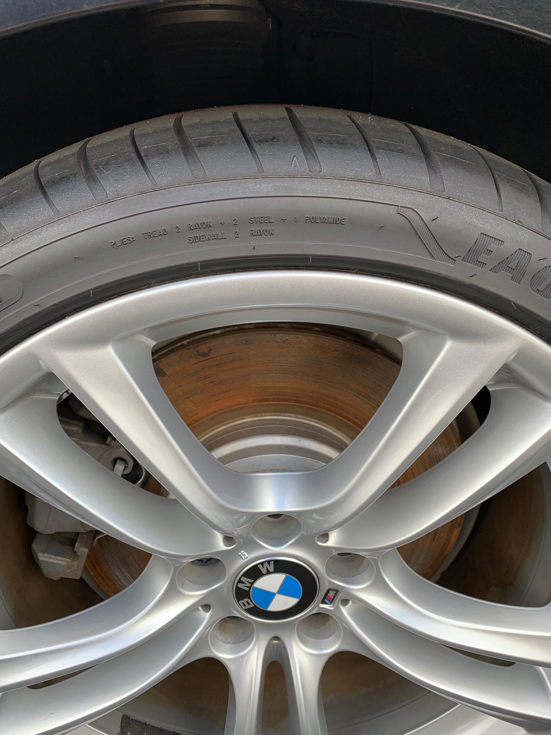 Close-up of a BMW wheel with silver alloy rim and rusty brake disc underneath.