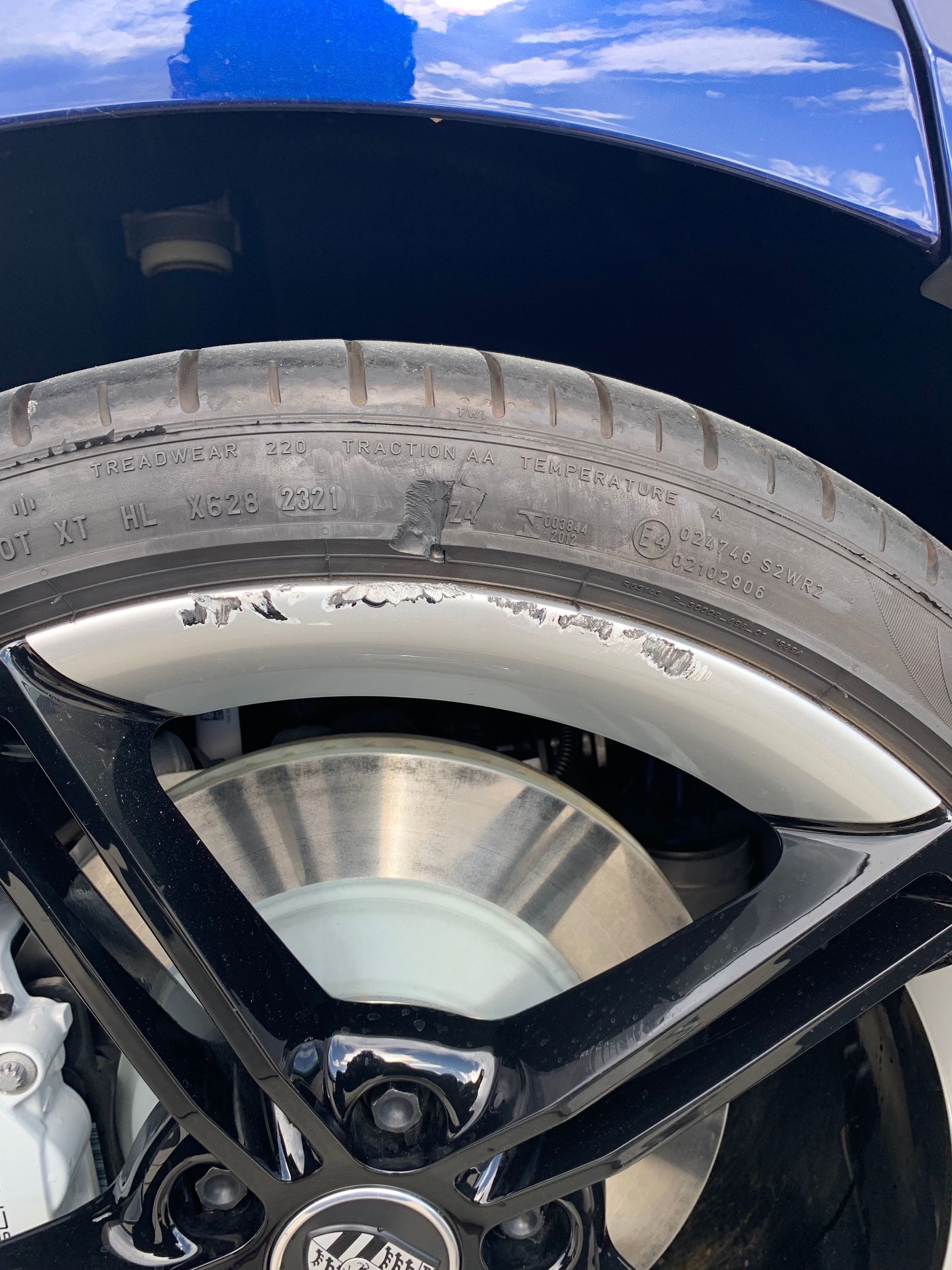 Close-up of a car wheel and tire with visible scuffing on the wheel arch, under a blue fender.