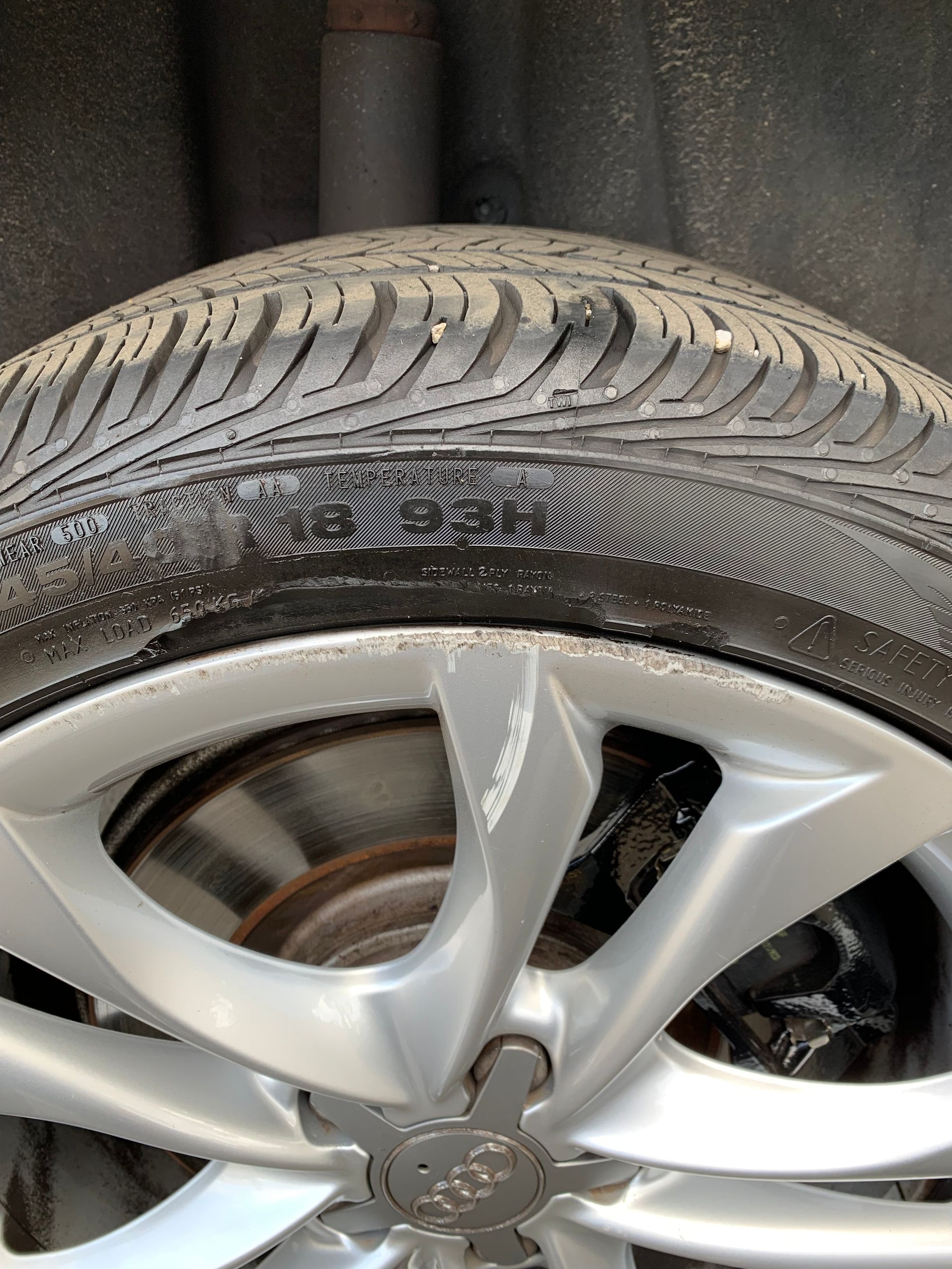 Close-up of a silver car wheel and tire, showing tire tread and rim damage from curb scraping.