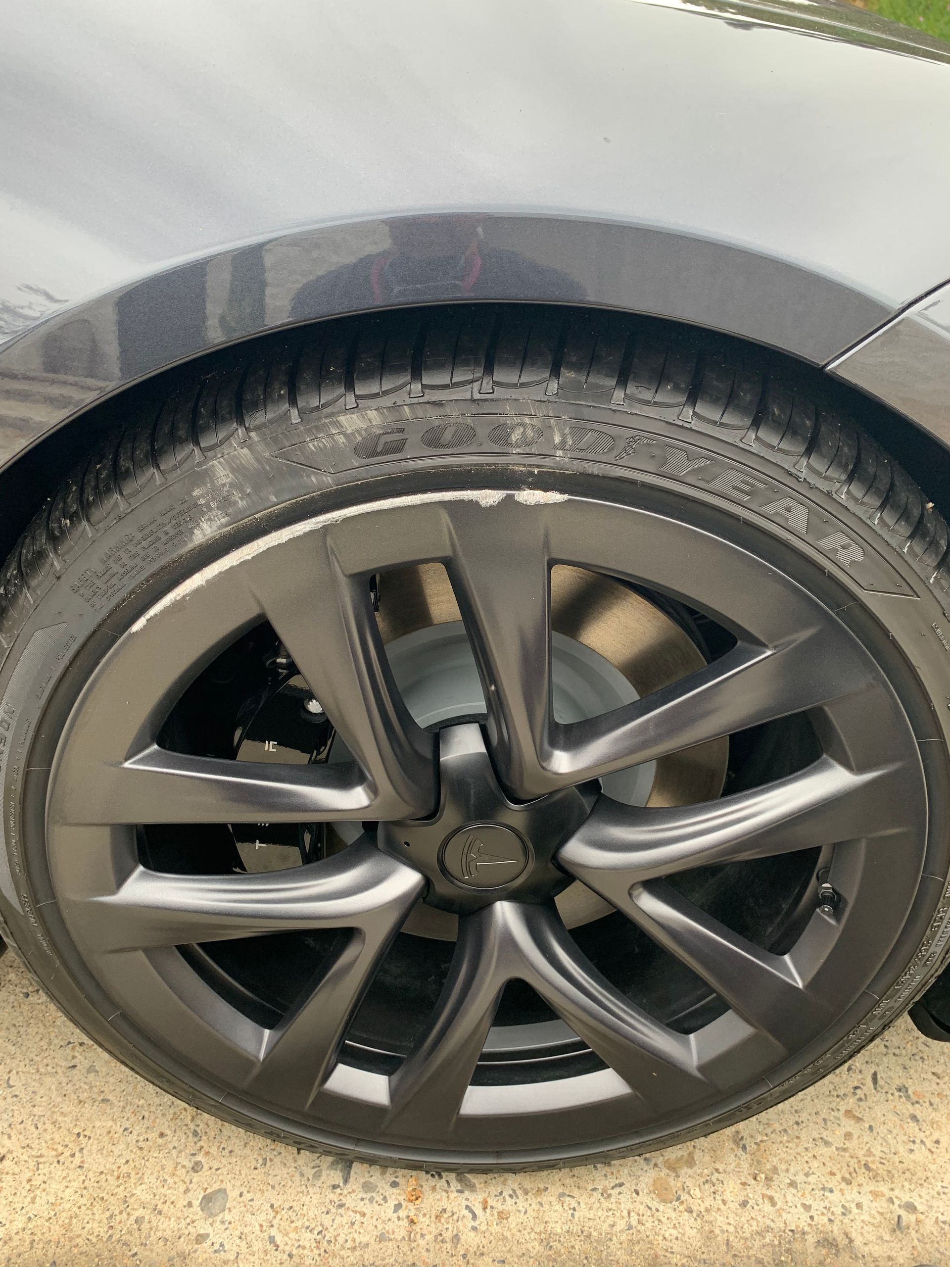 Close-up of a car’s front wheel with a dark alloy rim and tire, parked on pavement.
