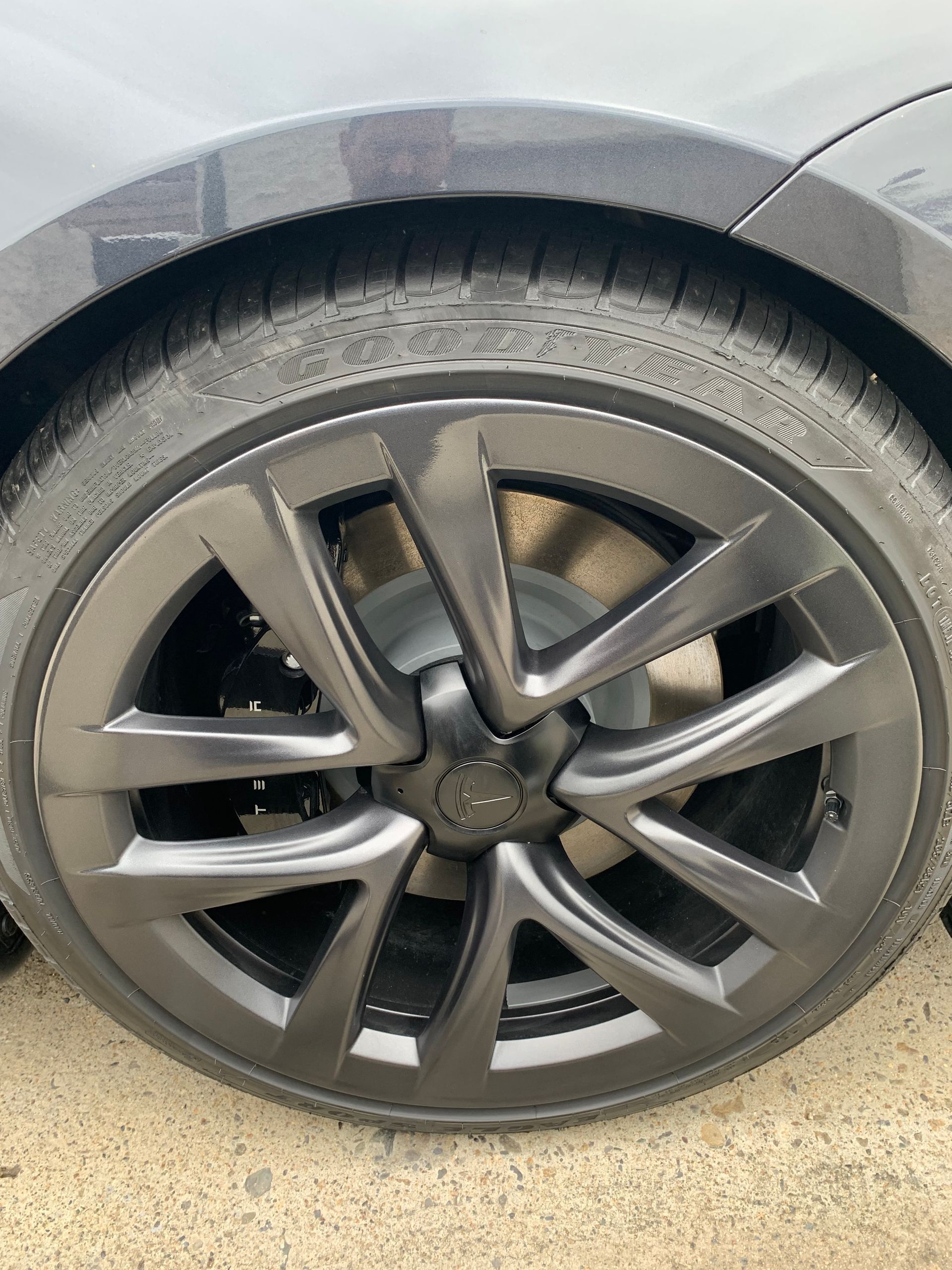 Close-up of a gray car’s front wheel and tire with alloy rim and visible tread.