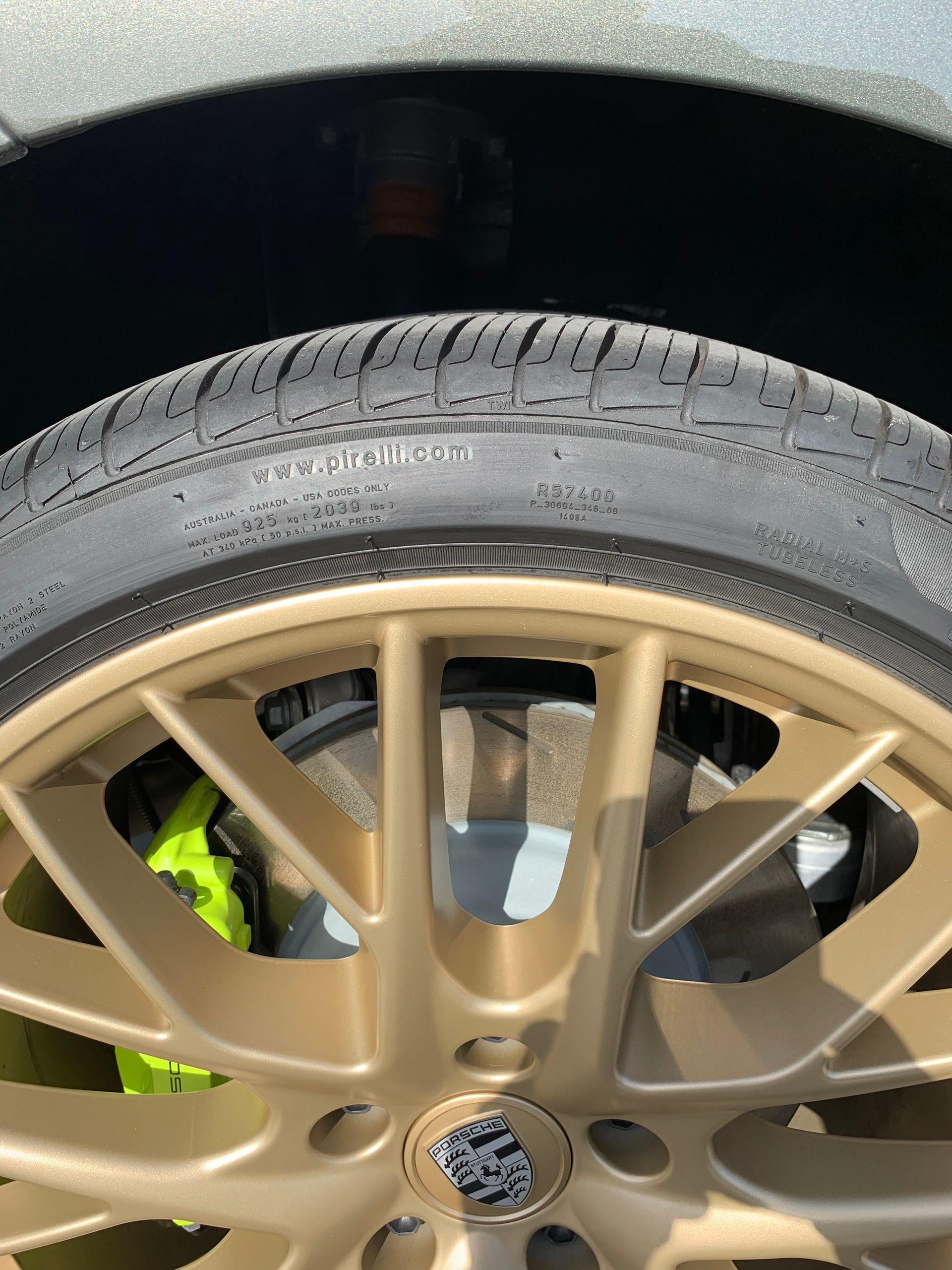 Close-up of a gold alloy car wheel with a black tire and bright green brake caliper underneath.