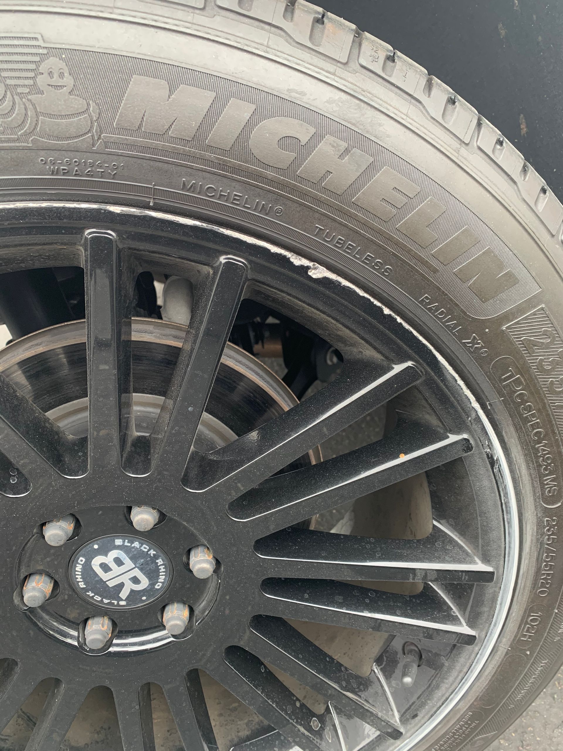 Close-up of a black car wheel with a tire and silver lug nuts showing wear and dirt.