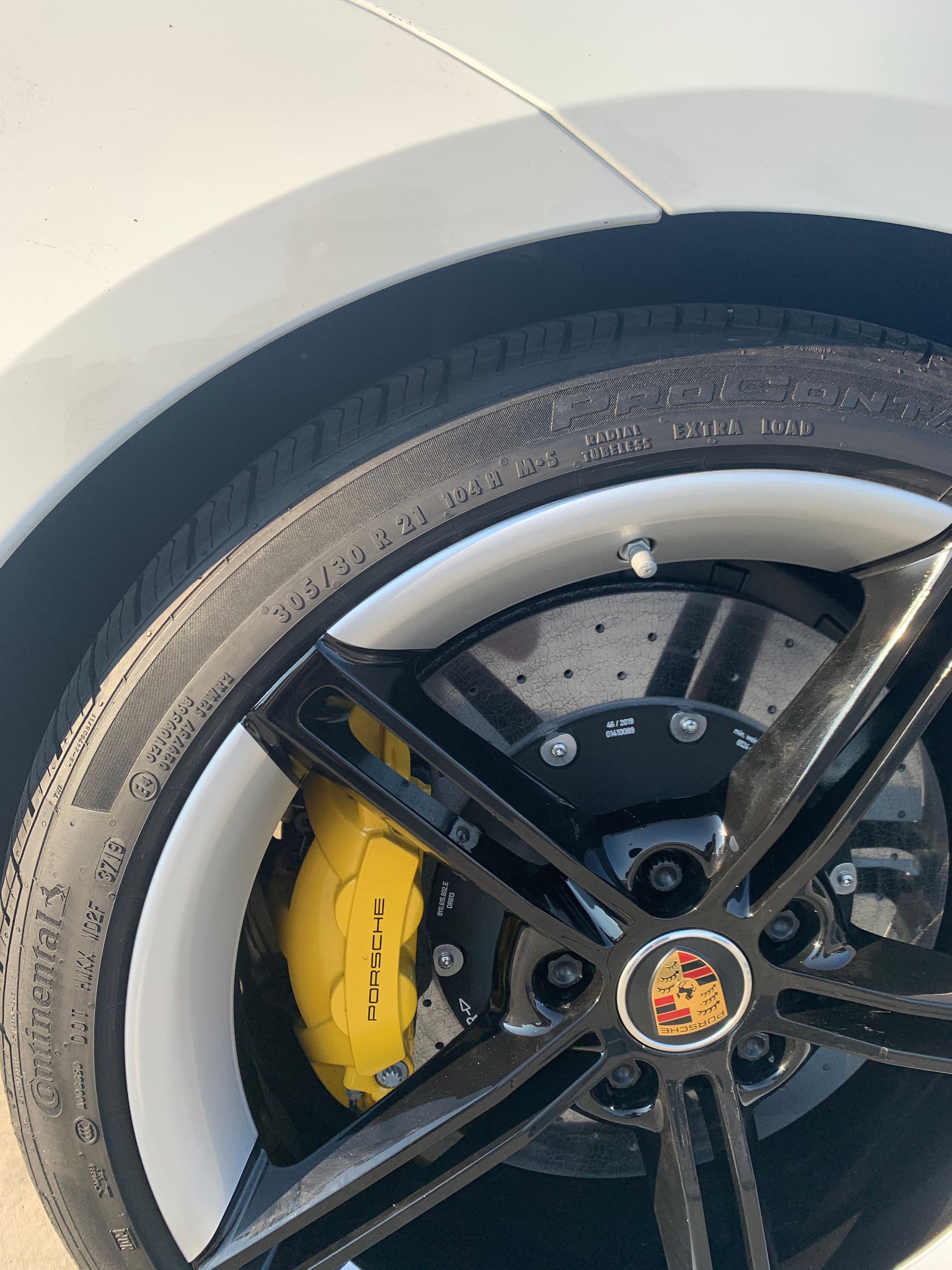 Close-up of a car wheel with black rim, yellow brake caliper, and white body panel.