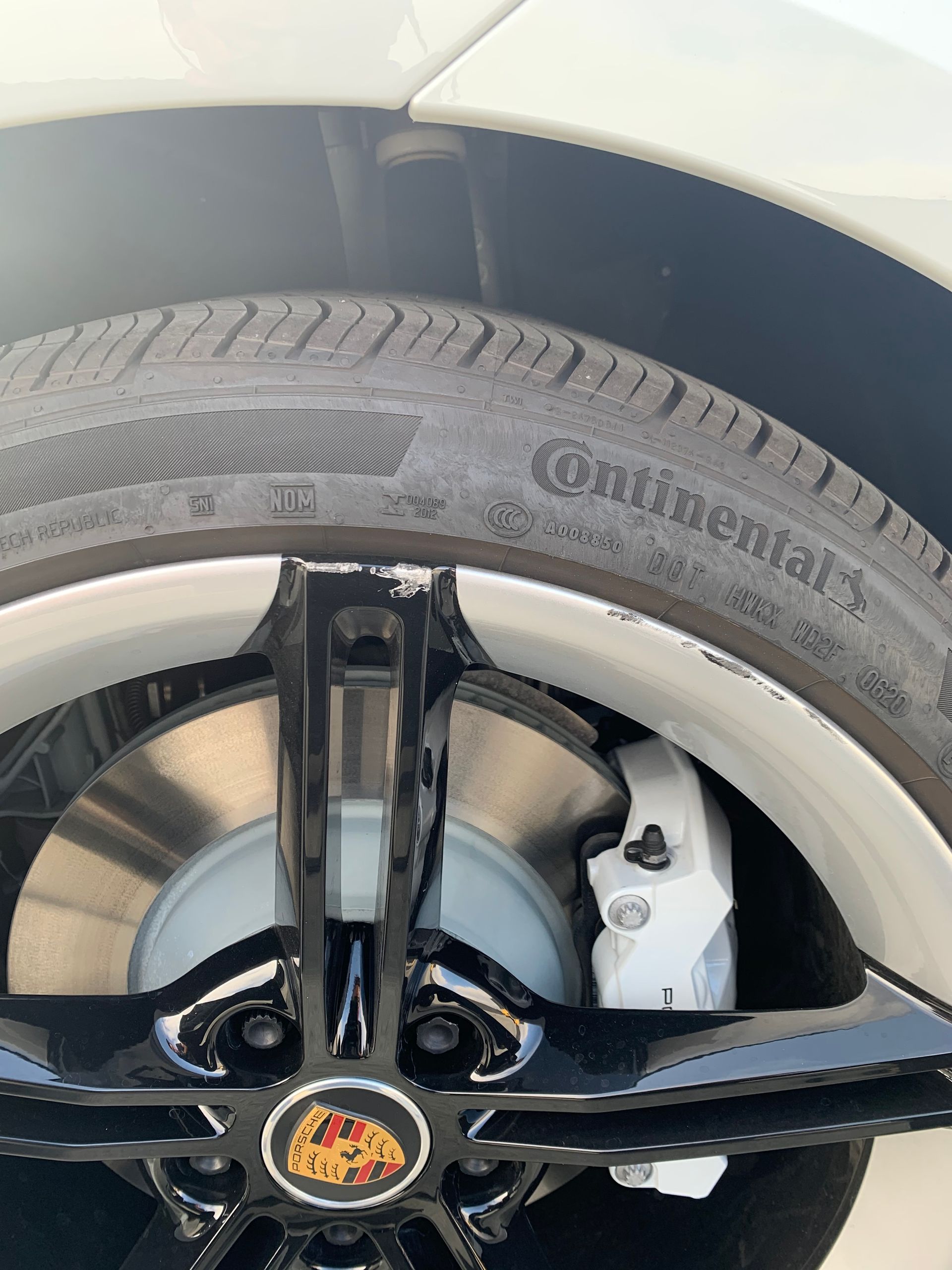 Close-up of a car wheel and tire with a black rim and white brake caliper, showing a Porsche emblem.