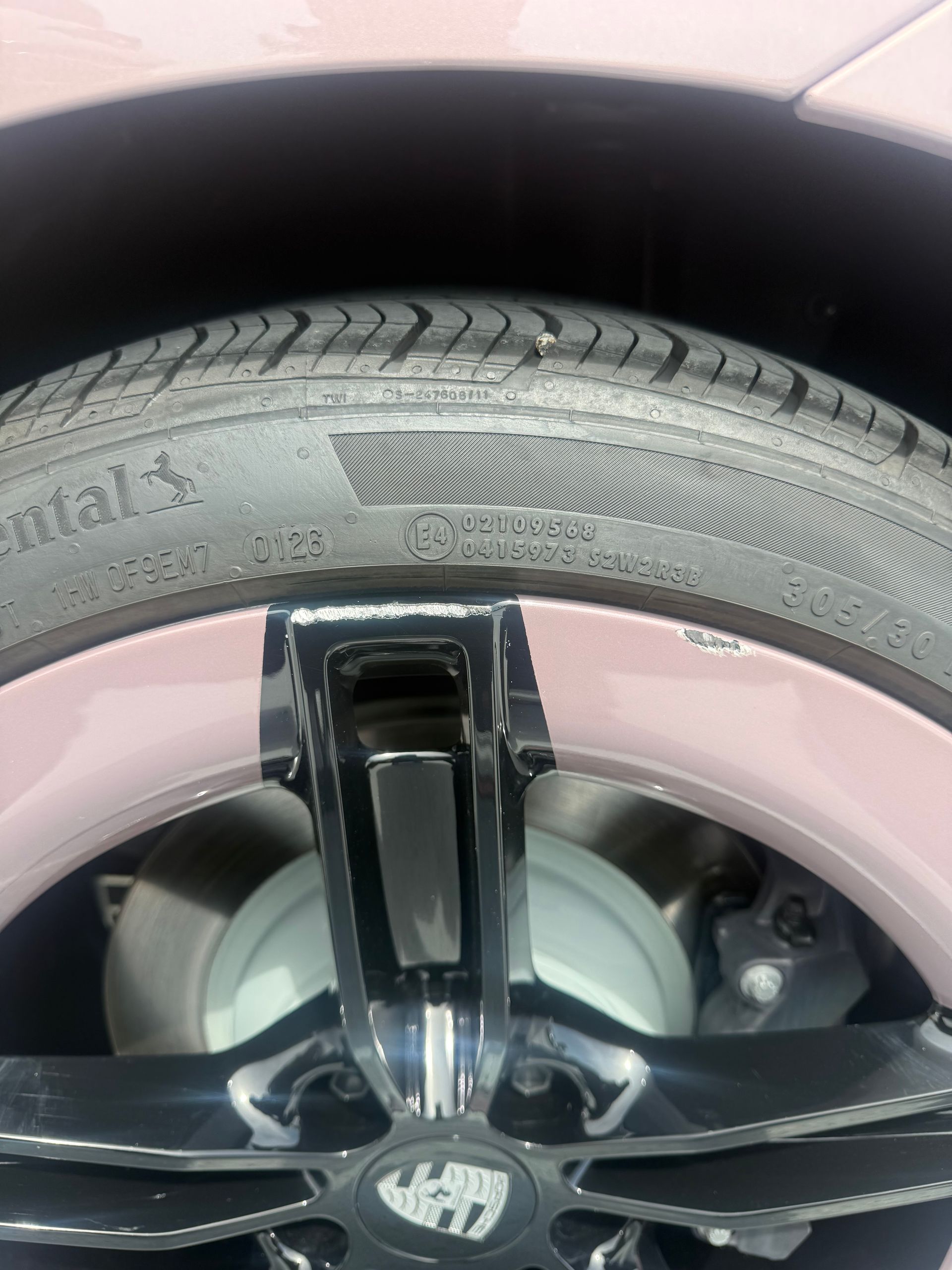 Close-up of a black car wheel and tire with visible sidewall damage and scratches on the rim.