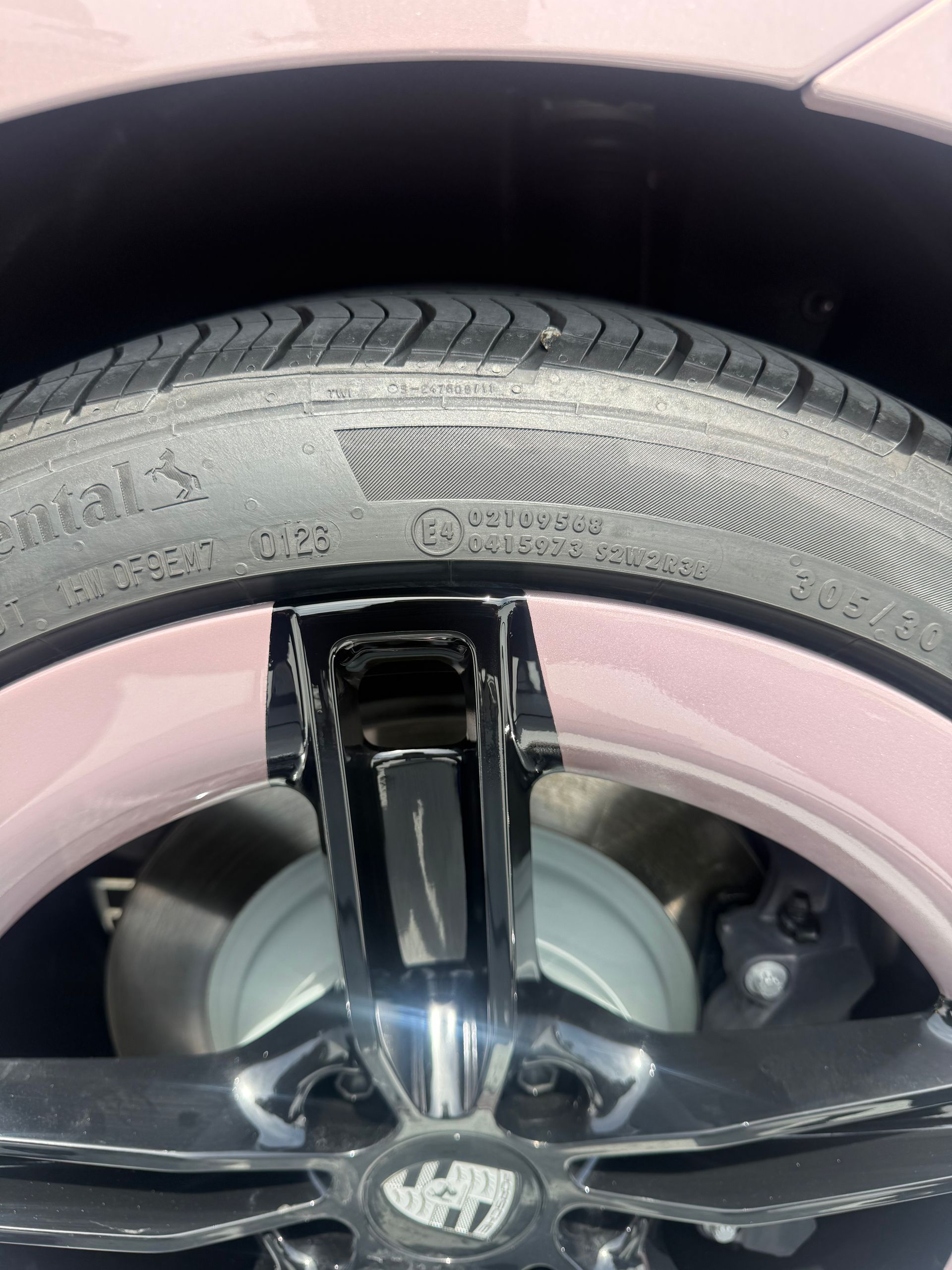 Close-up of a car wheel and tire with a pink rim and black five-spoke rim.