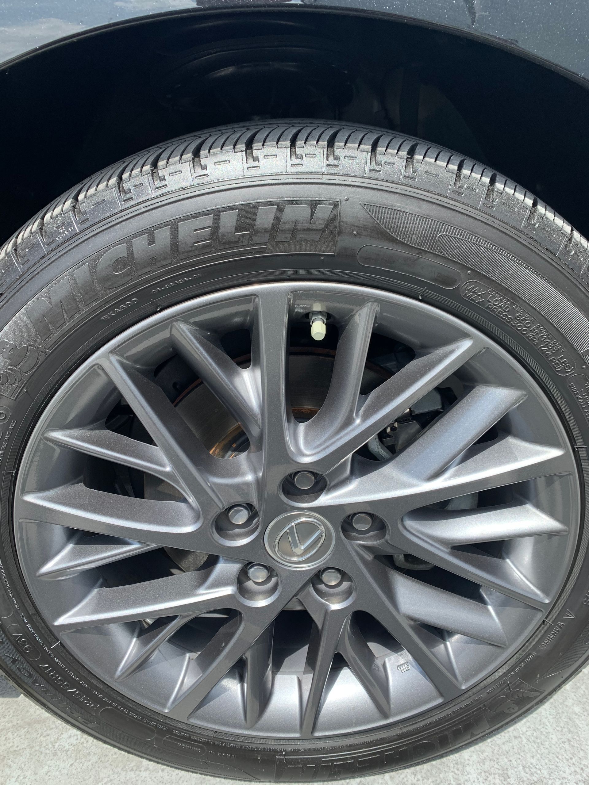 Close-up of a car wheel with a silver alloy rim and black tire on a dark body panel.