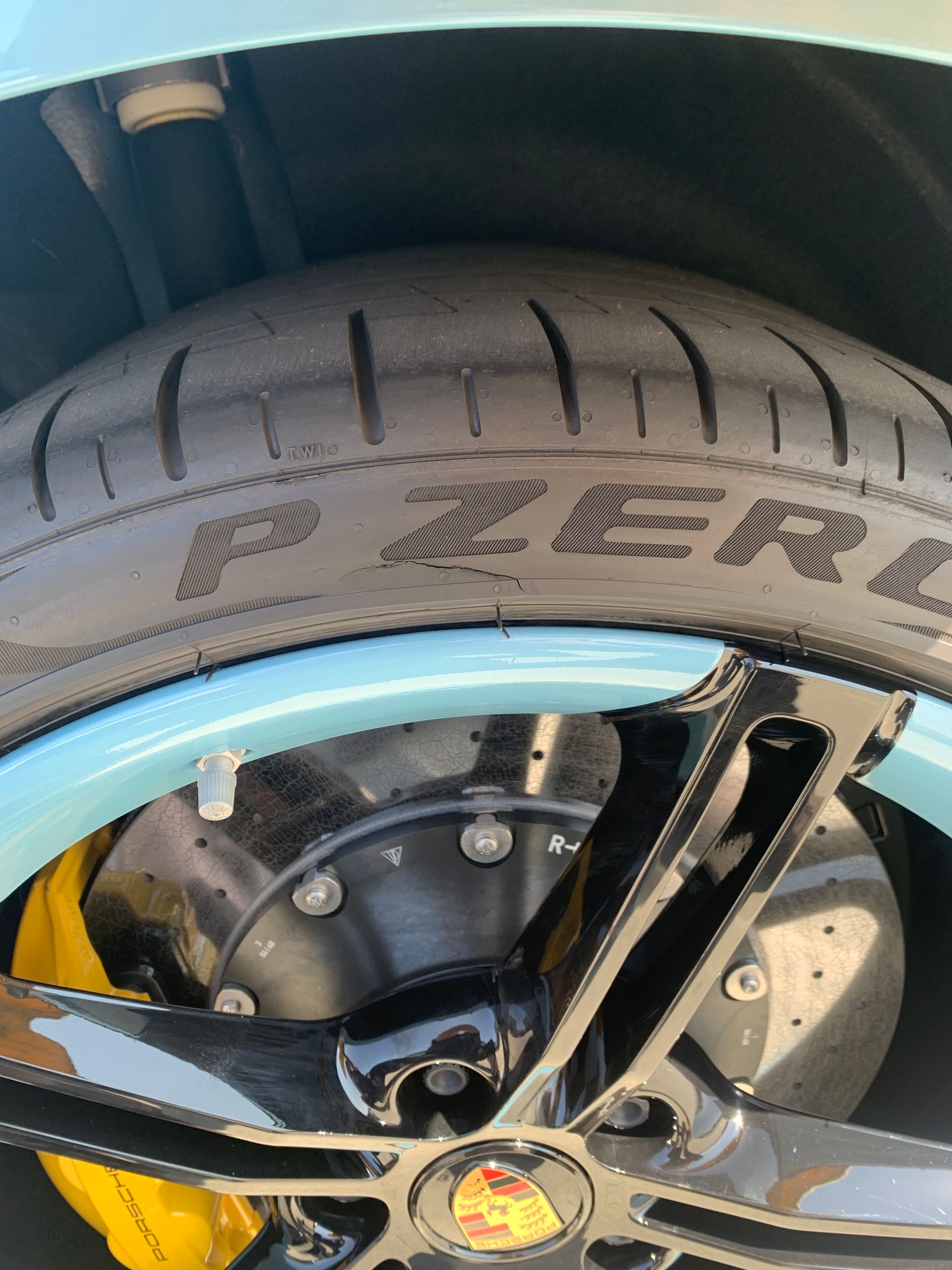 Close-up of a car wheel with a black tire, silver rim, and blue fender accent.