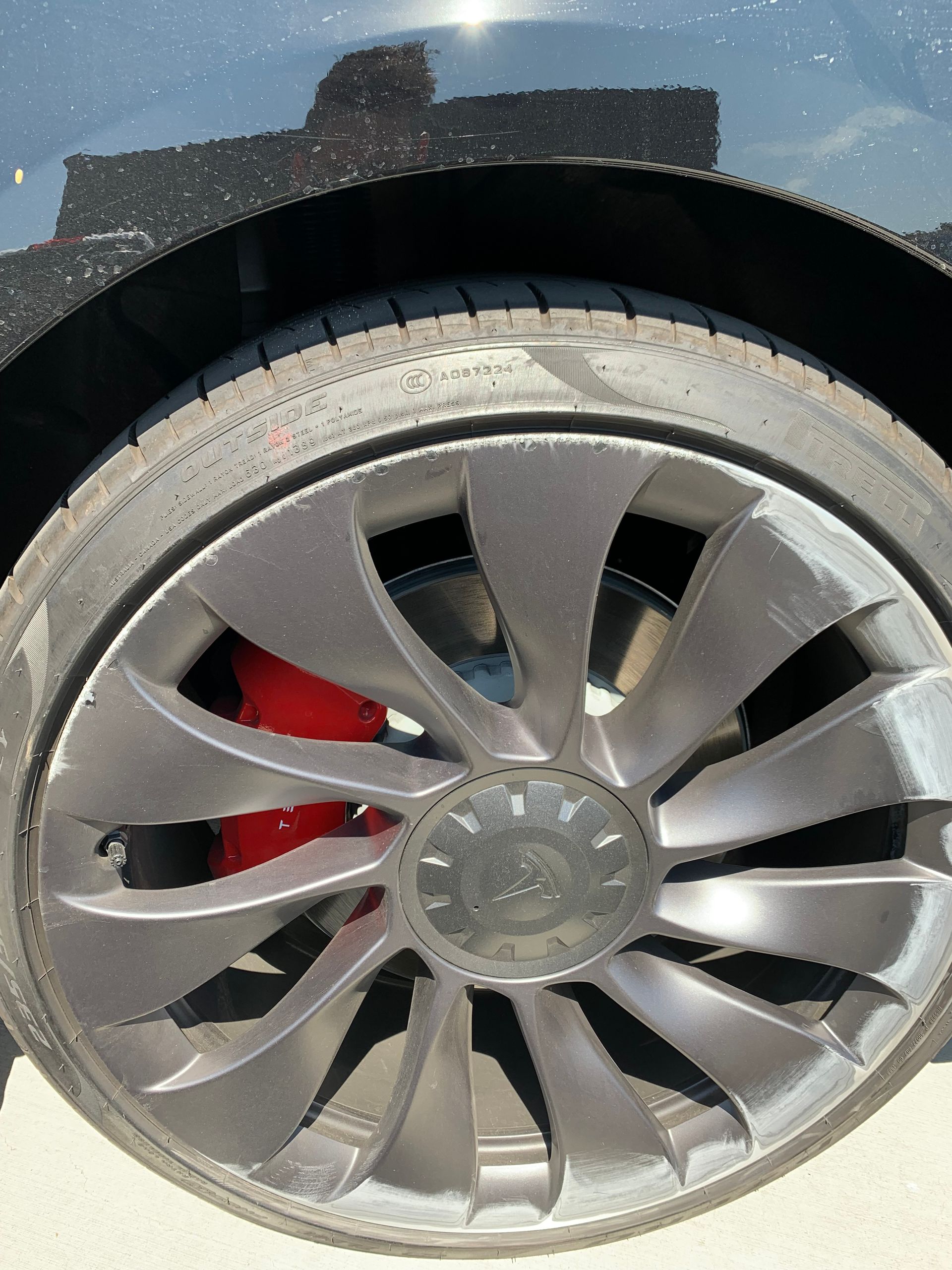 Close-up of a car wheel with a silver rim and red brake caliper behind it, slightly dusty.
