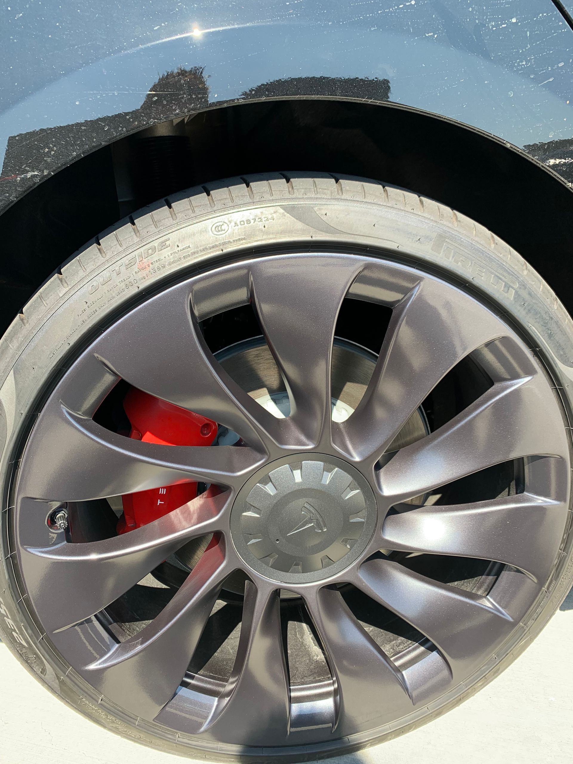 Close-up of a car wheel with a silver alloy rim and red brake caliper against a dark body panel.