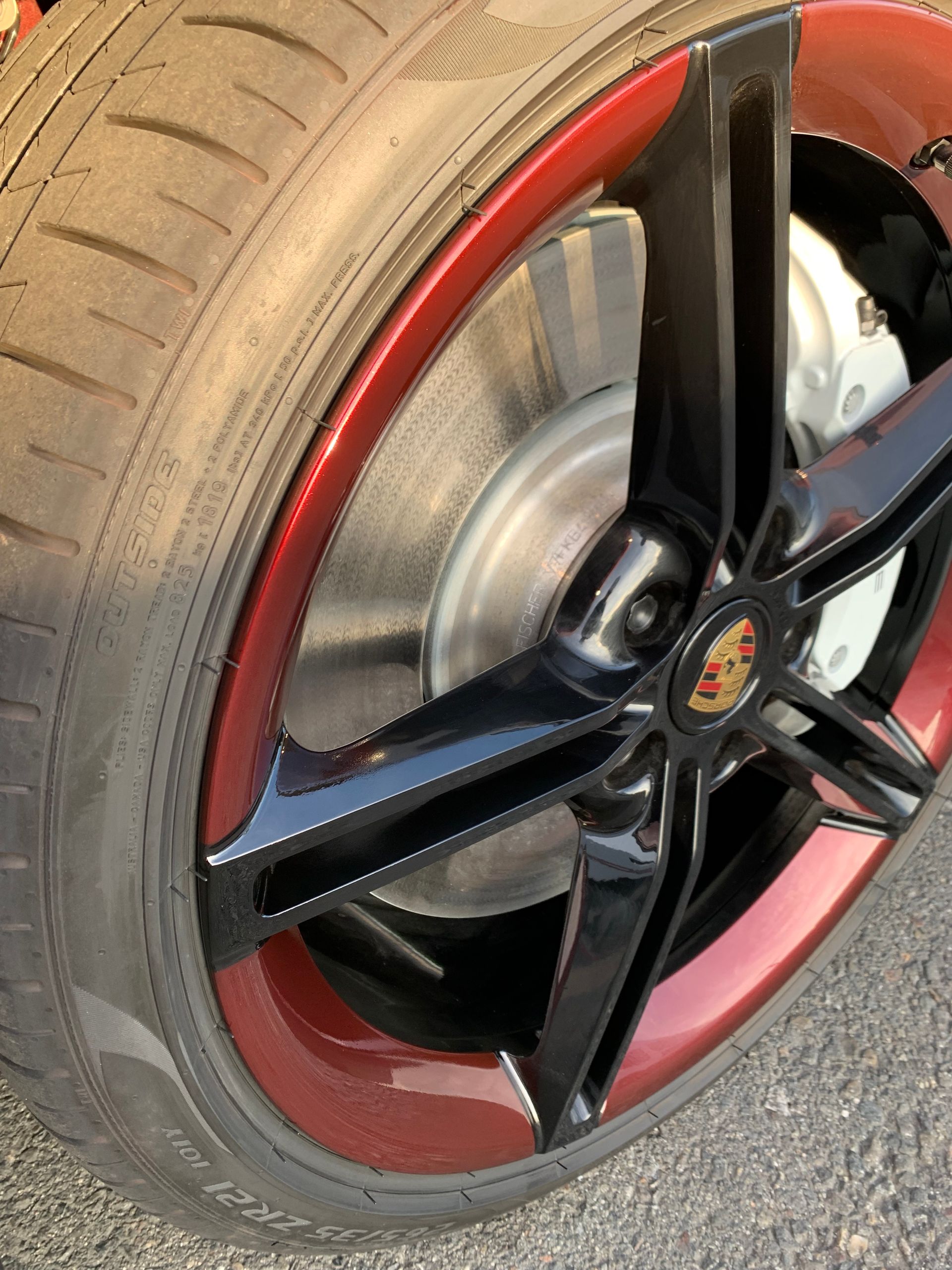 Close-up of a black and red car wheel with a Porsche center cap on the road.