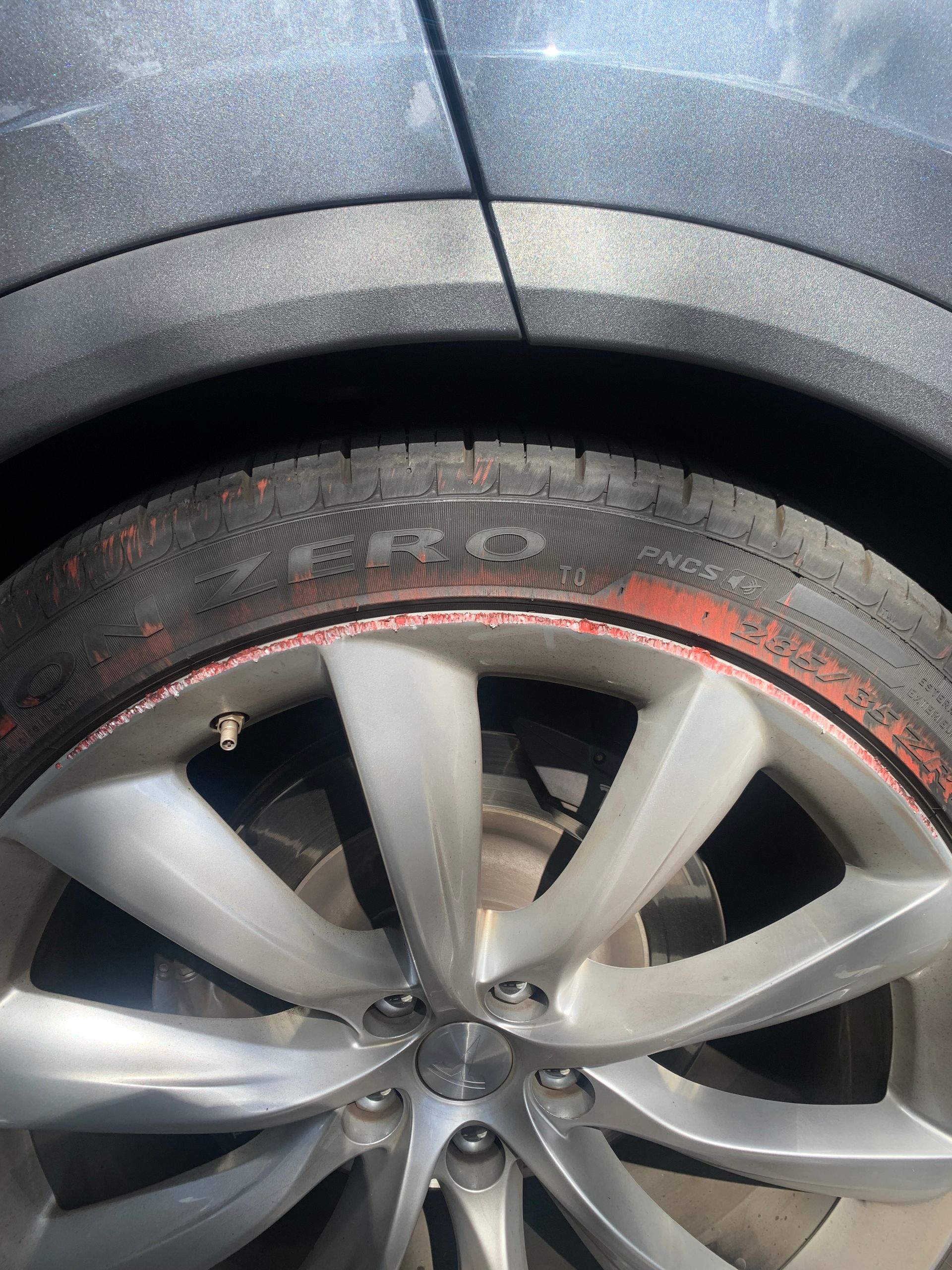 Close-up of a car wheel with a flat tire and a damaged, dusty rim against a dark fender.