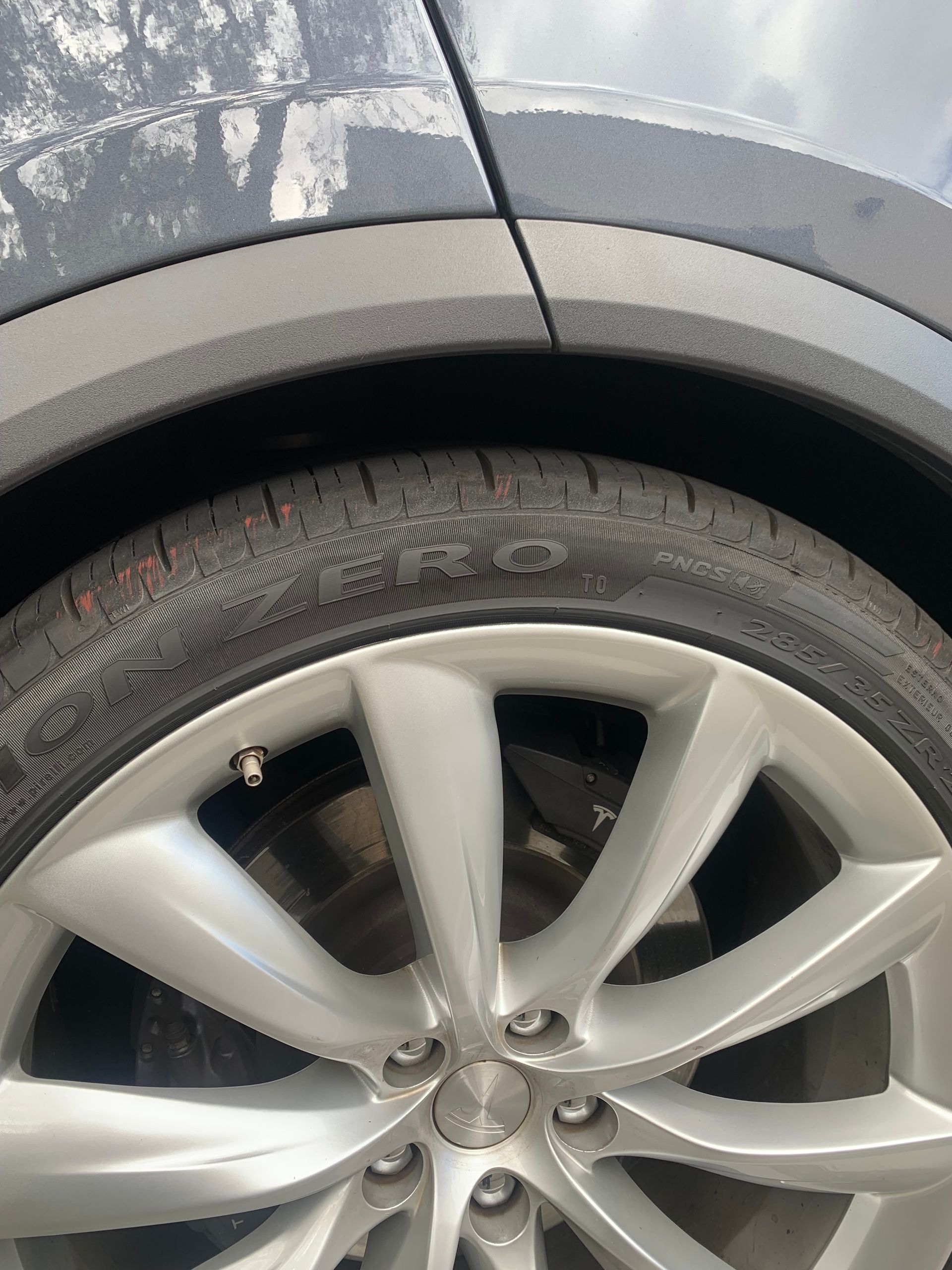 Close-up of a silver car wheel and tire beside a gray body panel with a small scratch.