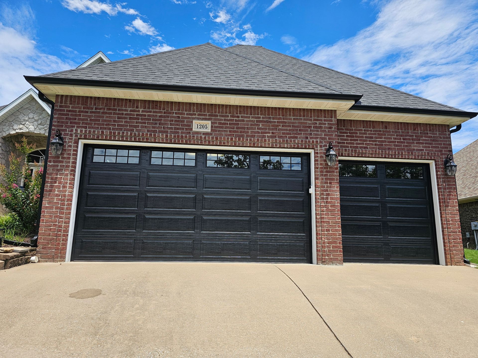 A brick house with two black garage doors on a sunny day.
