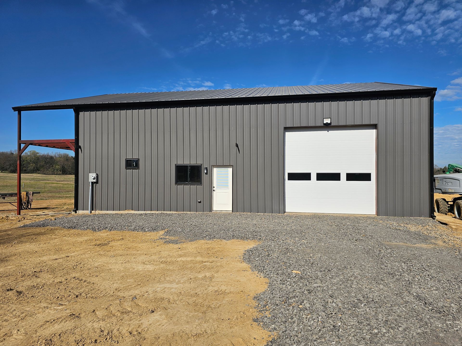 A large metal building with a white garage door is sitting on top of a gravel lot.