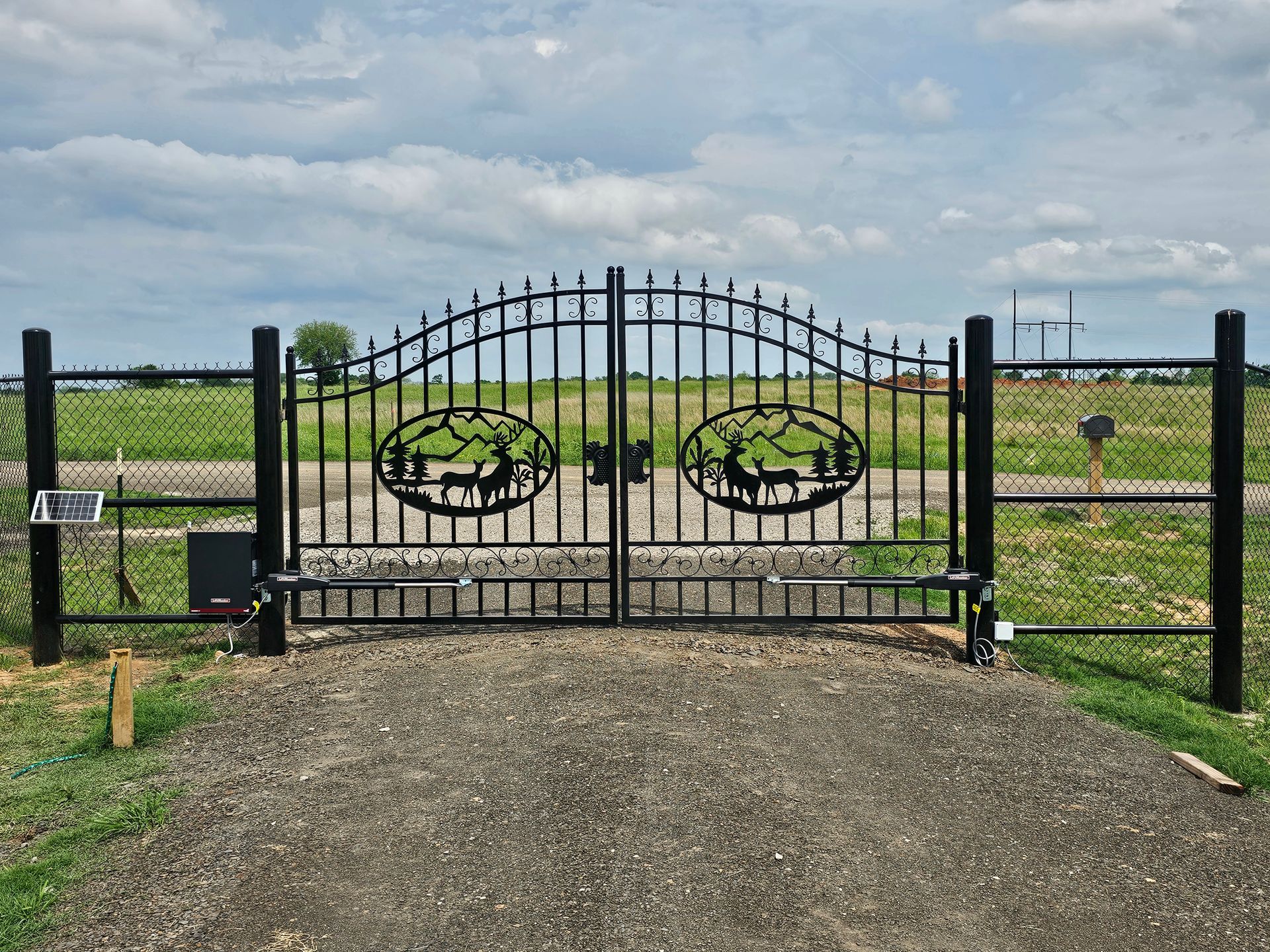 A black metal gate with a deer design on it is sitting on top of a gravel driveway.