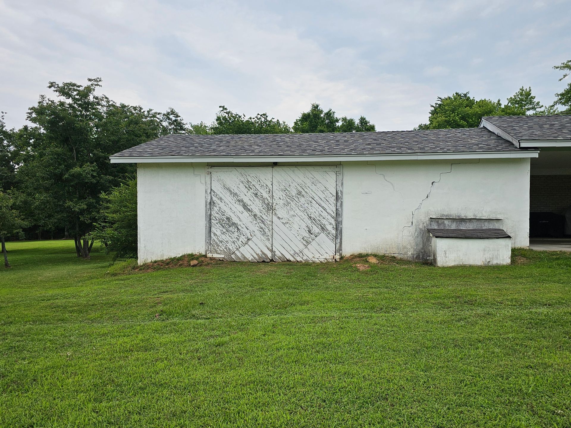 A white barn is sitting in the middle of a lush green field.