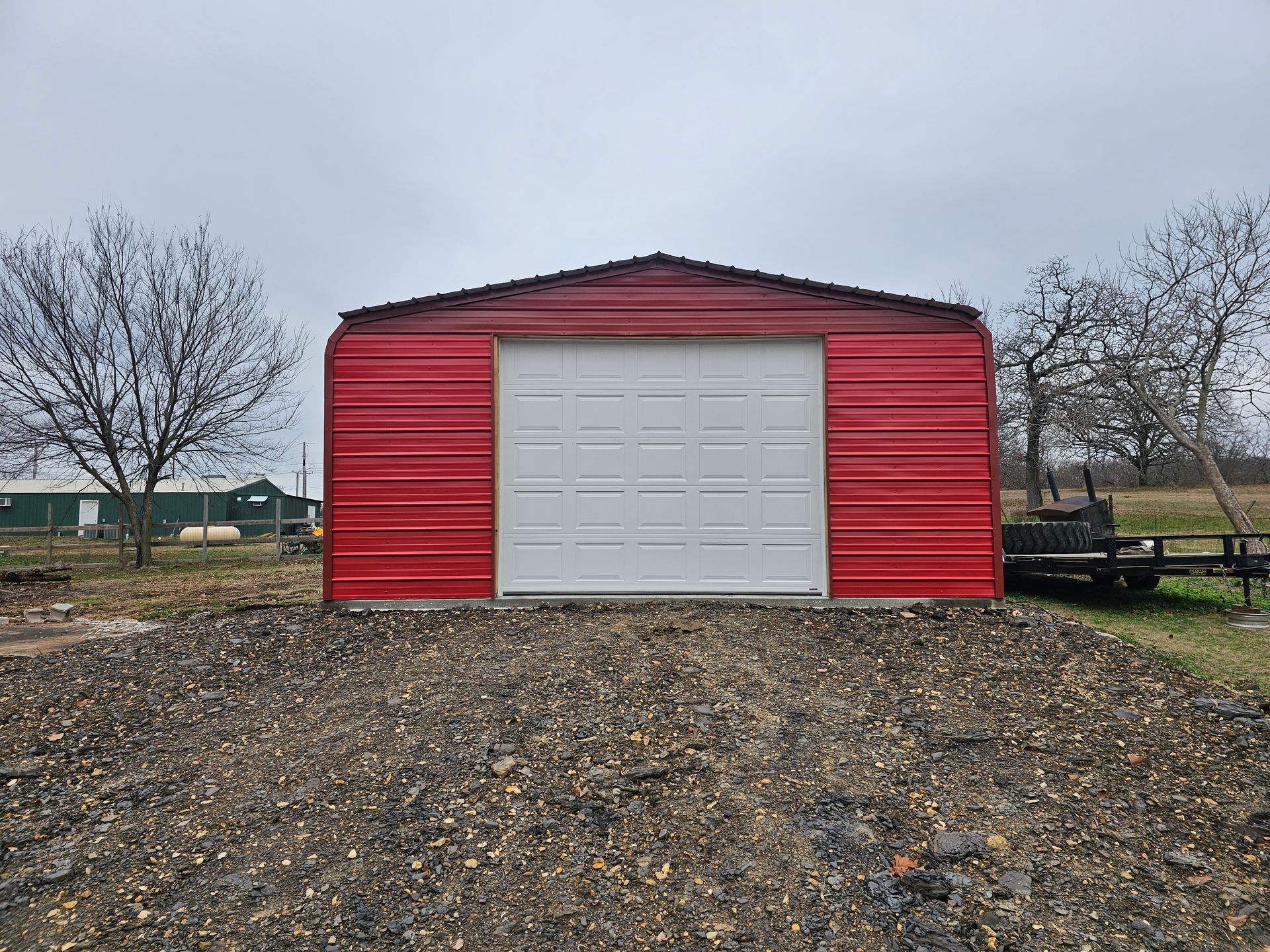 A red garage with a white garage door is sitting on top of a gravel lot.